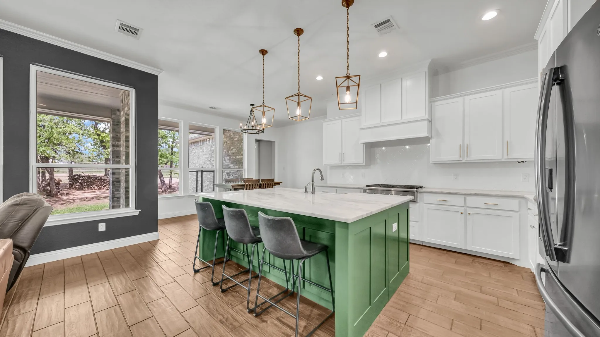 Two tone kitchen with freestanding refrigerator, dual tone cabinets, a kitchen island with sink, wood tiled floors, and ornamental molding