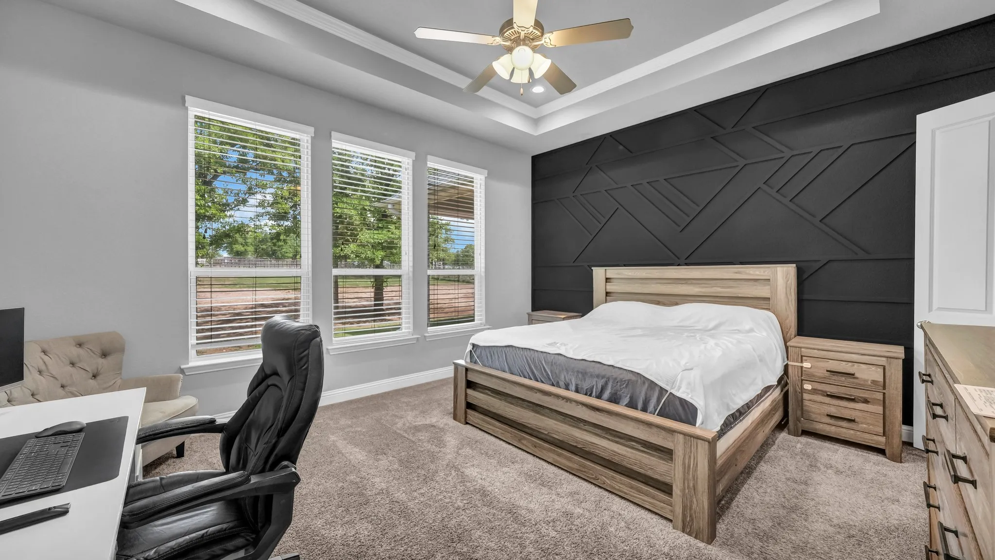 Carpeted bedroom with a desk, an accent wall, ceiling fan, a raised ceiling, and ornamental molding
