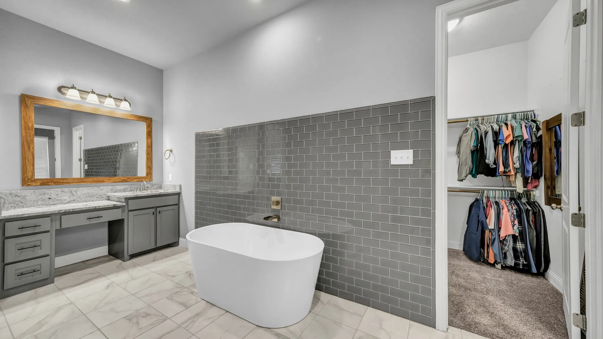 Bathroom featuring vanity, a soaking tub, a walk in closet, tile walls, and light marble finish floors