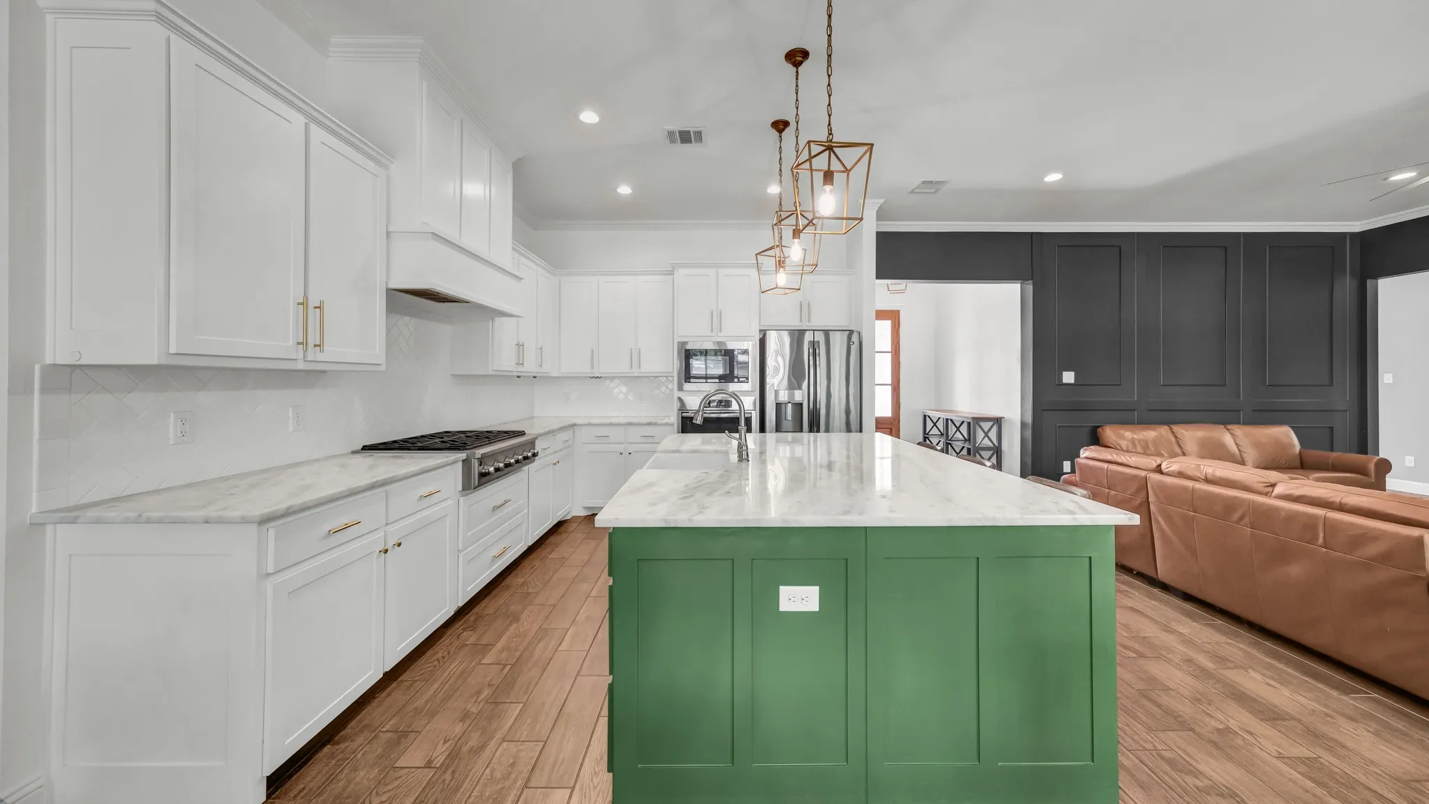 Dual tone kitchen with ornamental molding, light stone countertops, an island with sink, open floor plan, and stainless steel appliances