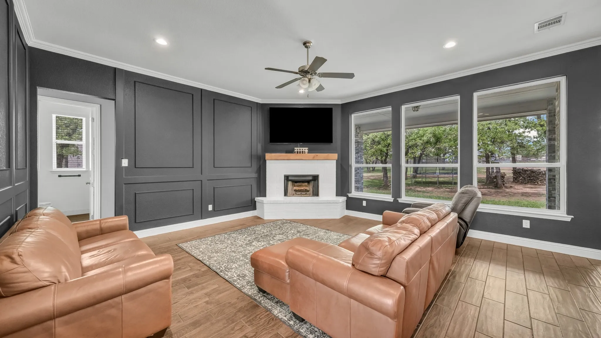 Living room featuring wood finish floors, a ceiling fan, a fireplace with raised hearth, recessed lighting, and ornamental molding
