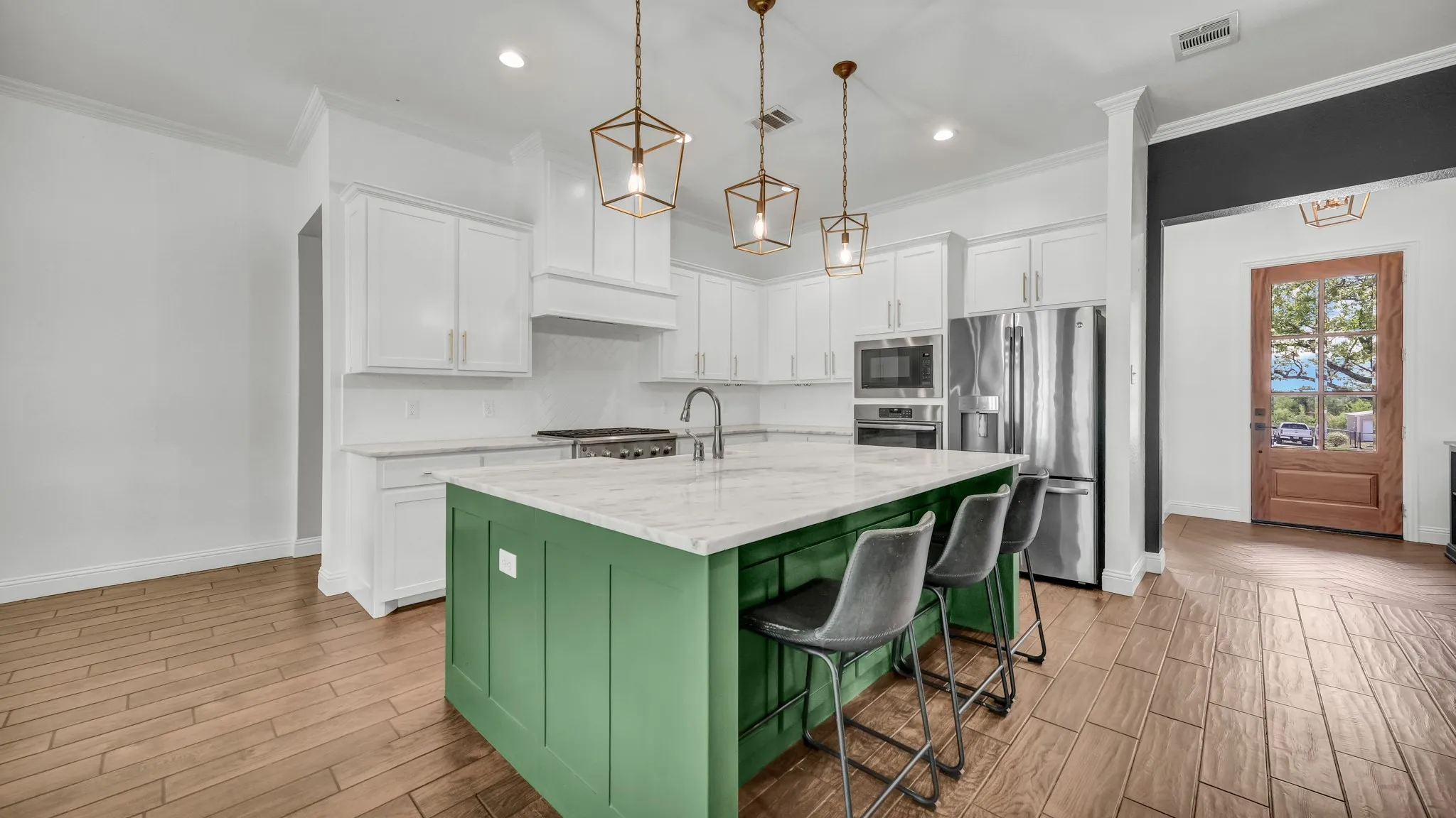 Two tone kitchen with wood finish floors, stainless steel appliances, a center island with sink, light stone countertops, and dual tone cabinets