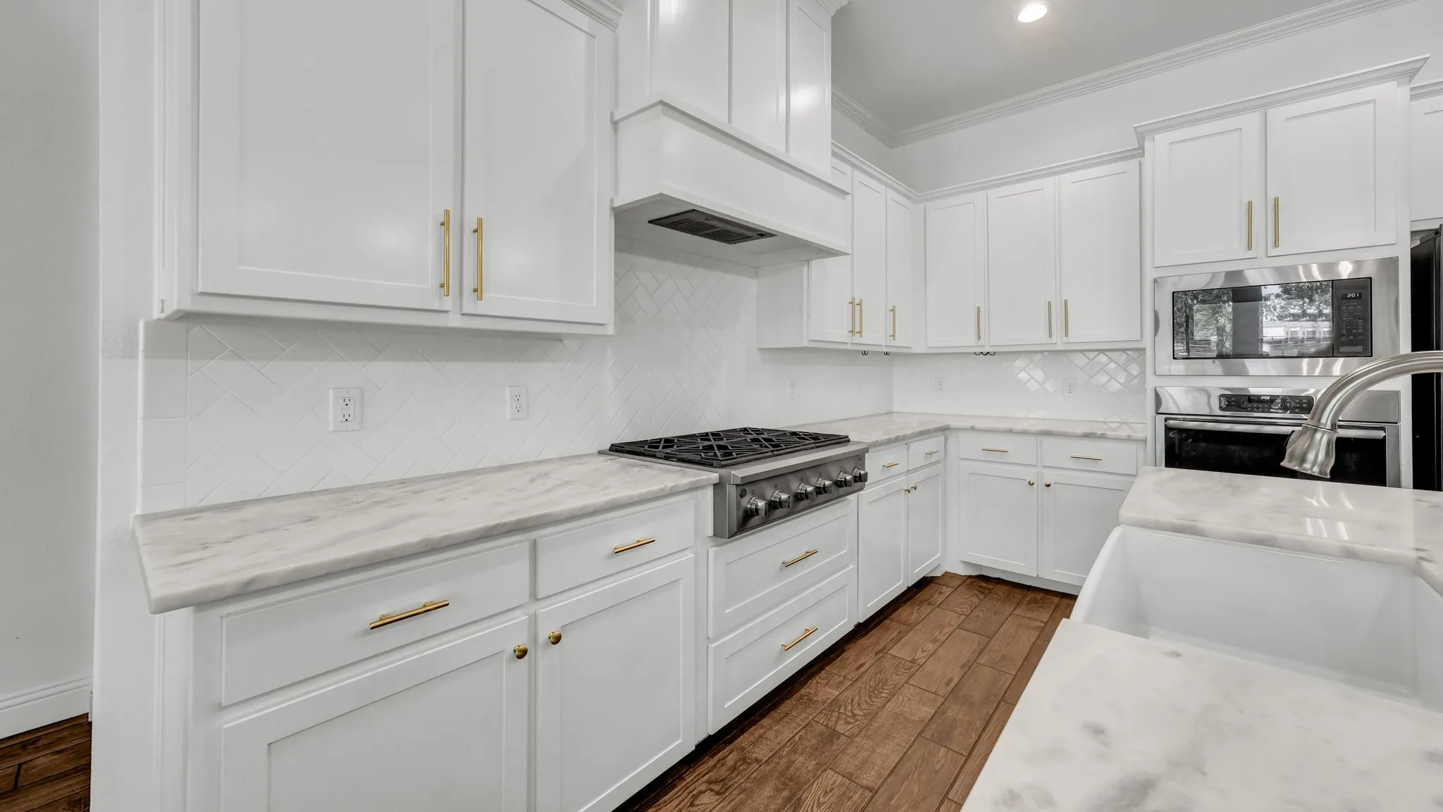 Kitchen with white cabinetry, dark wood-style floors, stainless steel appliances, light stone countertops, and ornamental molding