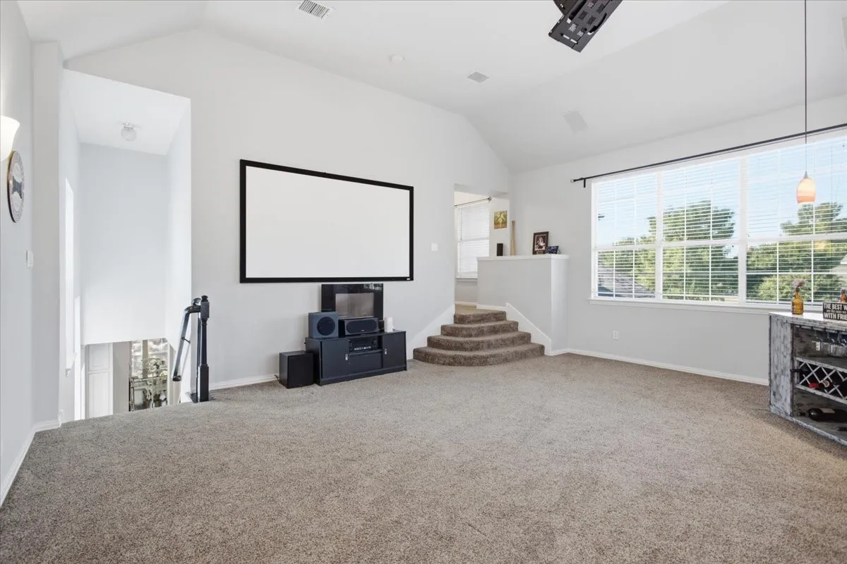 Spacious upstairs area featuring vaulted ceilings, plush carpeting, a built-in projection screen, and large windows with natural light