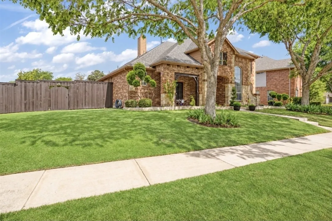 Brick and stone facade, covered porch entry, arched windows, manicured landscaping, and a wooden privacy fence