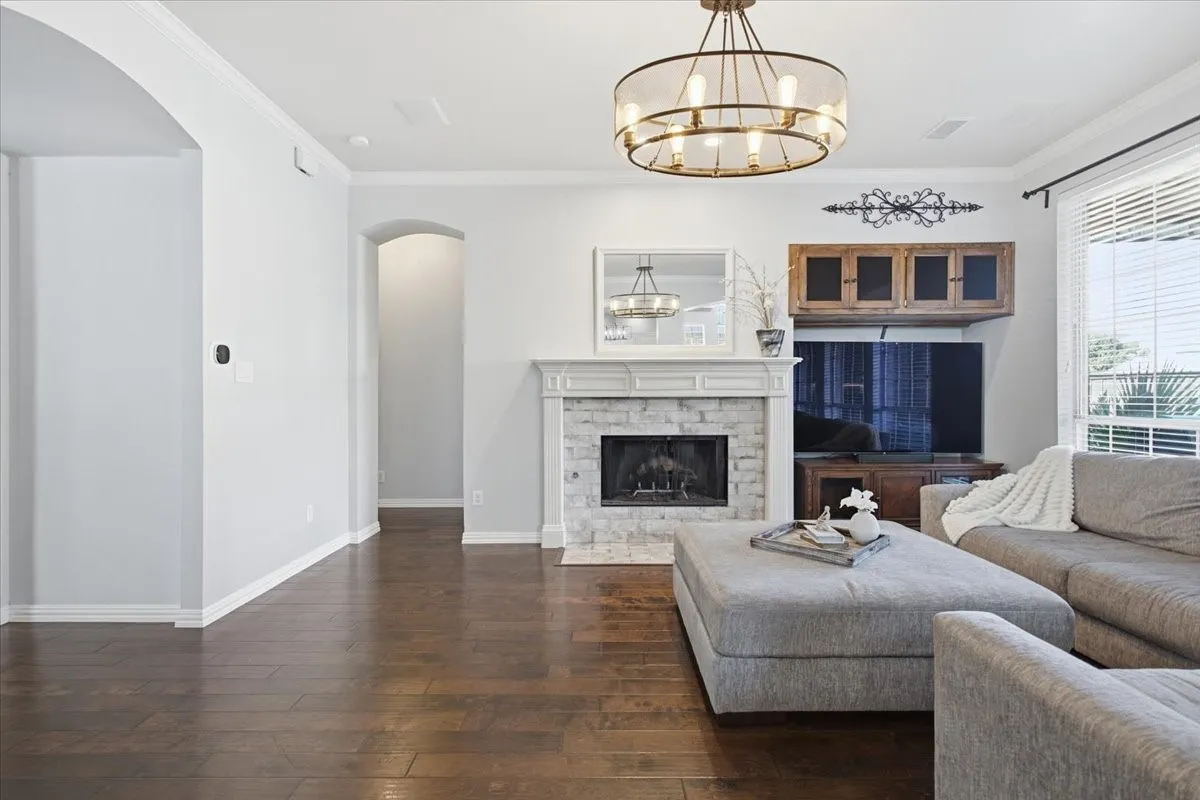 Dark wood-finish flooring, white stone fireplace with traditional mantel, arched doorways, a ceiling-mounted light fixture, and crown molding