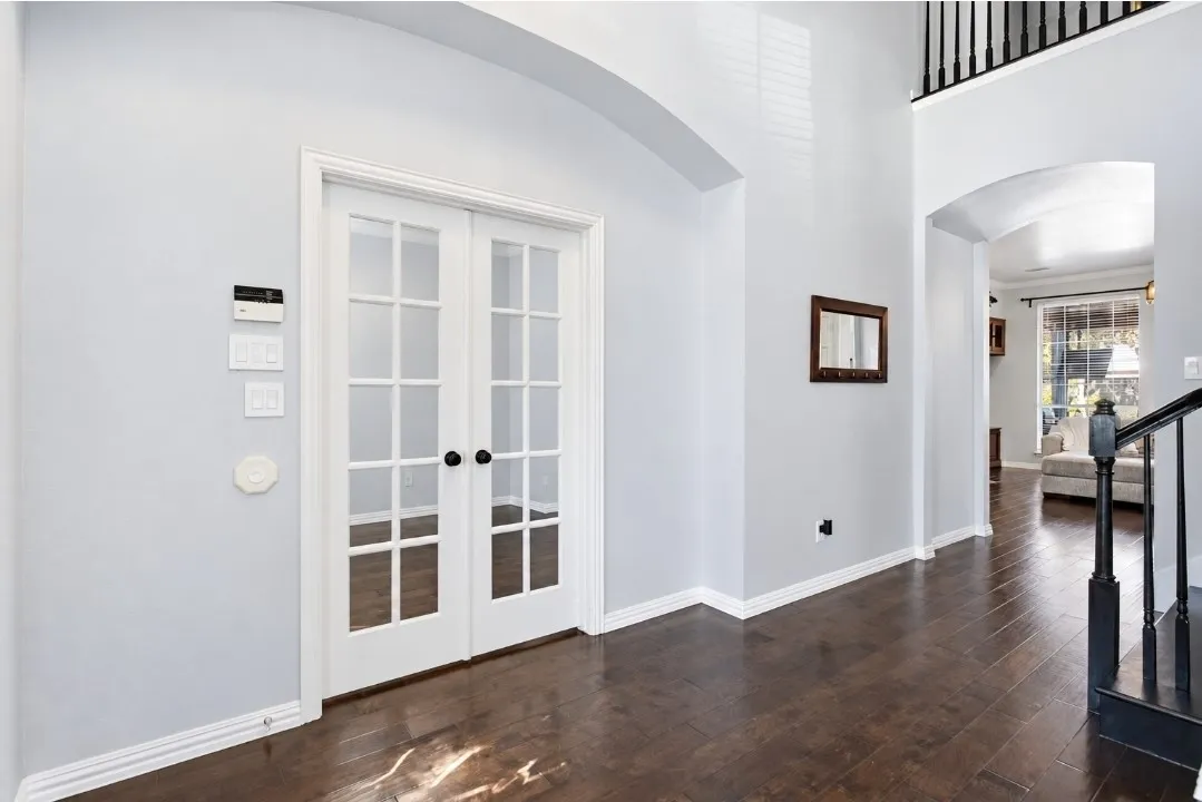 French doors with paneled glass, rich wood-finish flooring, white baseboards, arched doorways, and a dark wood handrail with balusters