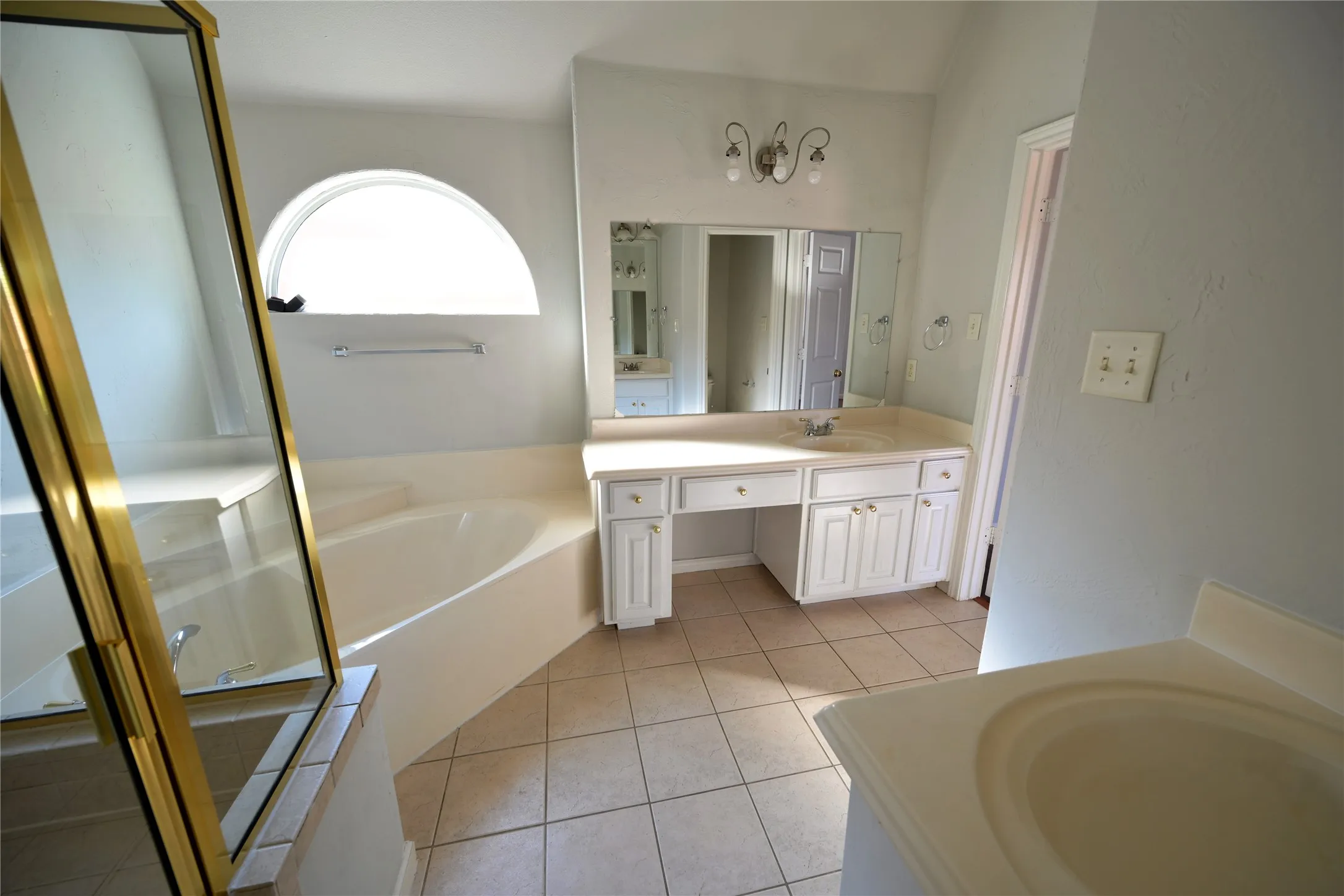 Bathroom featuring a soaking tub, arched window, tile flooring, and a vanity with integrated sink and built-in cabinetry