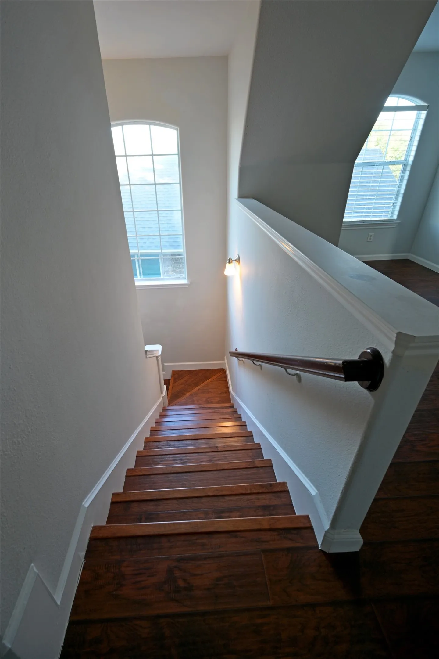 Staircase featuring wood-finish treads, a contrasting handrail, and a tall arched window