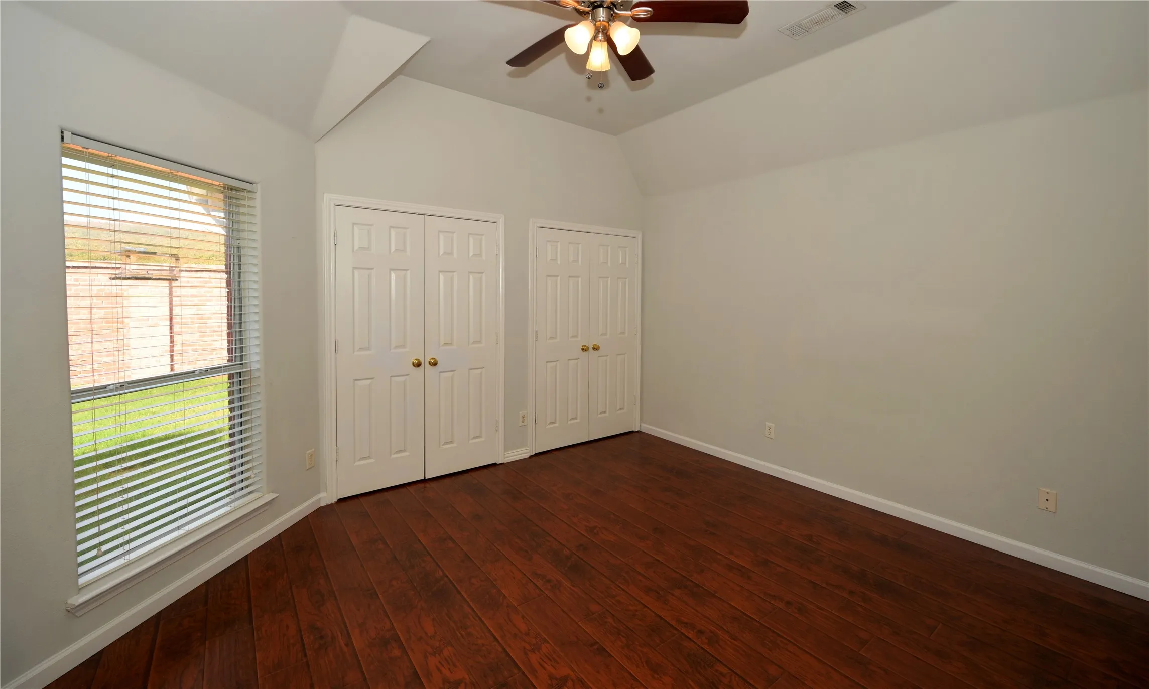 Room featuring vaulted ceilings, wood-finish flooring, and multiple bi-fold closets