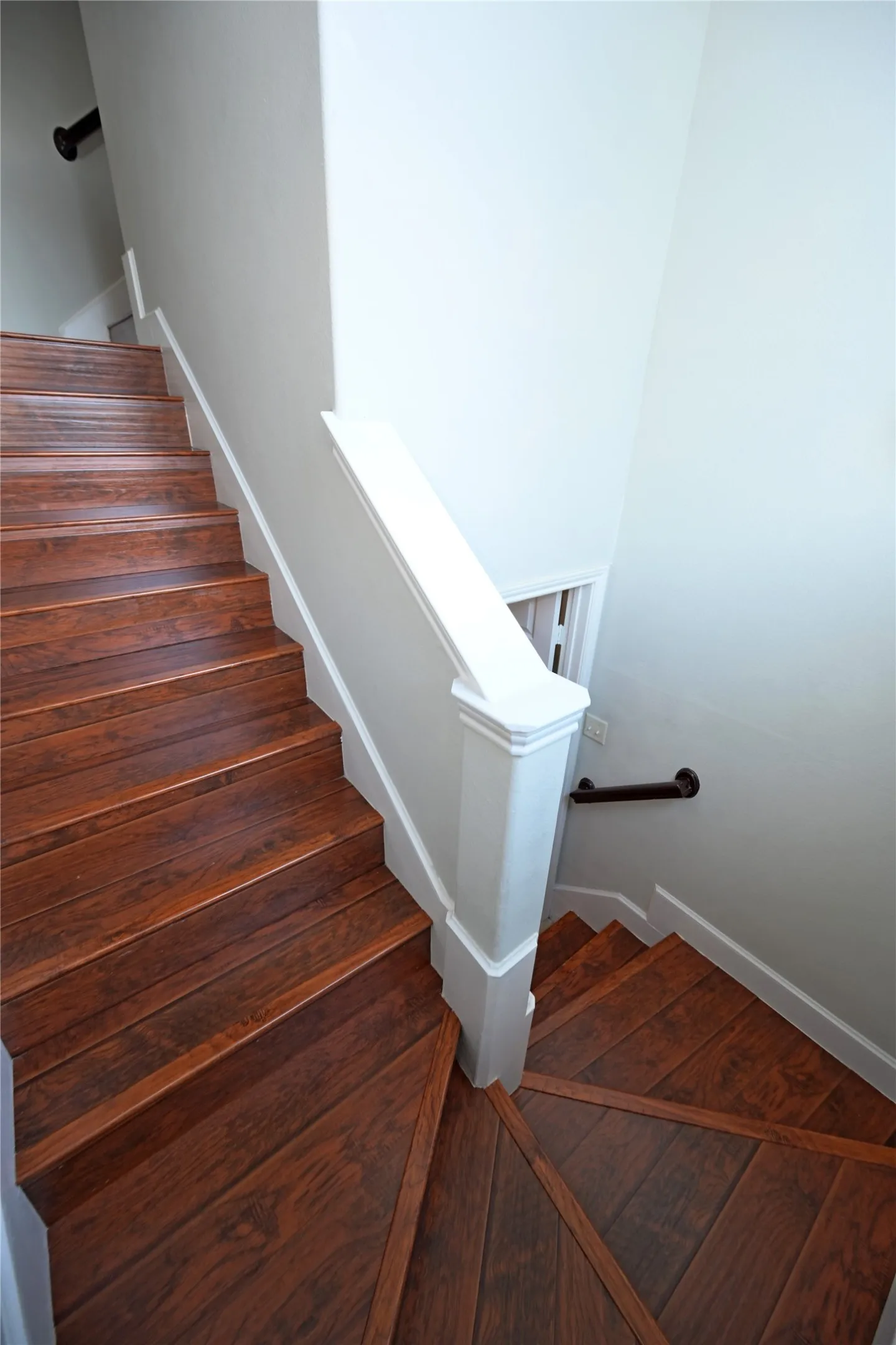 Hardwood staircase featuring a prominent newel post and white painted risers