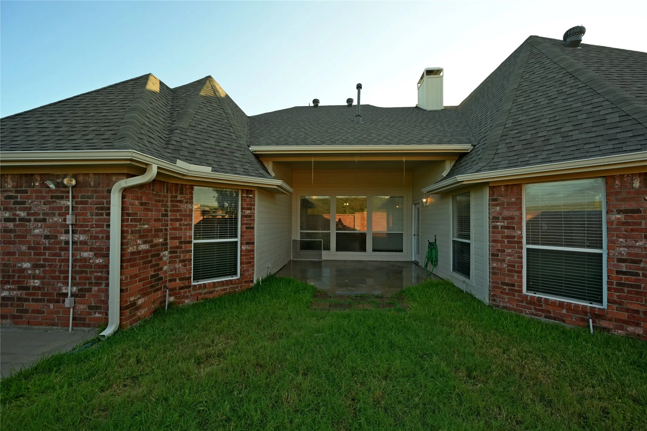 Rear exterior featuring a covered patio, brick and siding facade, and multiple windows