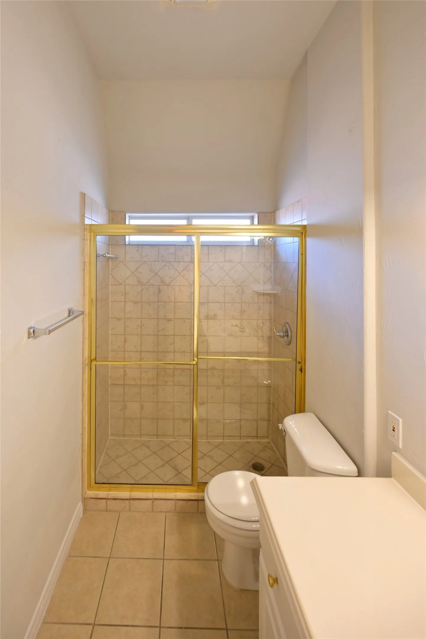 Shower stall with gold-tone framed glass enclosure and tiled interior, featuring a built-in shelf