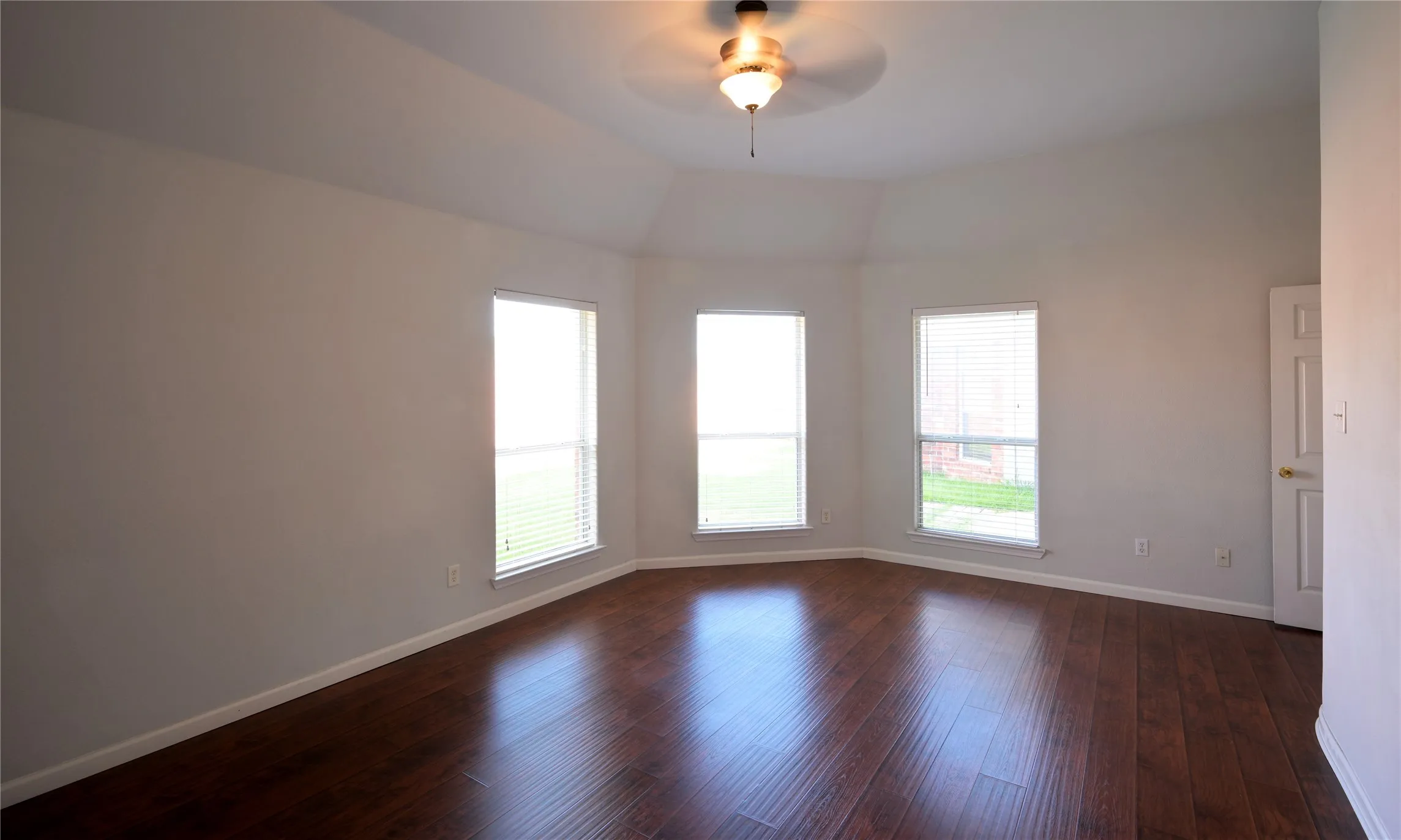 Spacious room featuring wood-finish flooring, vaulted ceiling, and a ceiling fan with integrated lighting