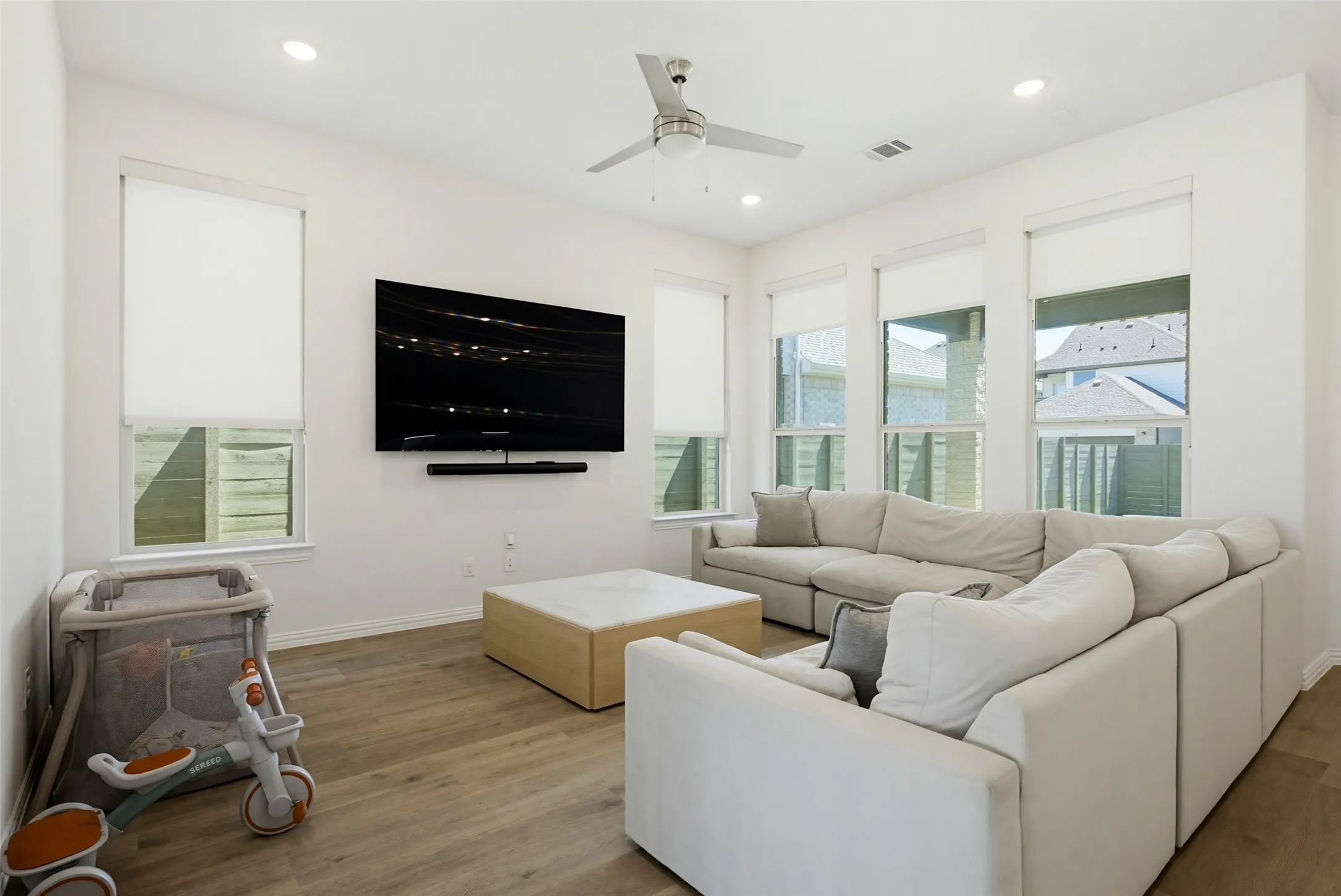Living area featuring wood-finish flooring, recessed lighting, and multiple windows with roller shades