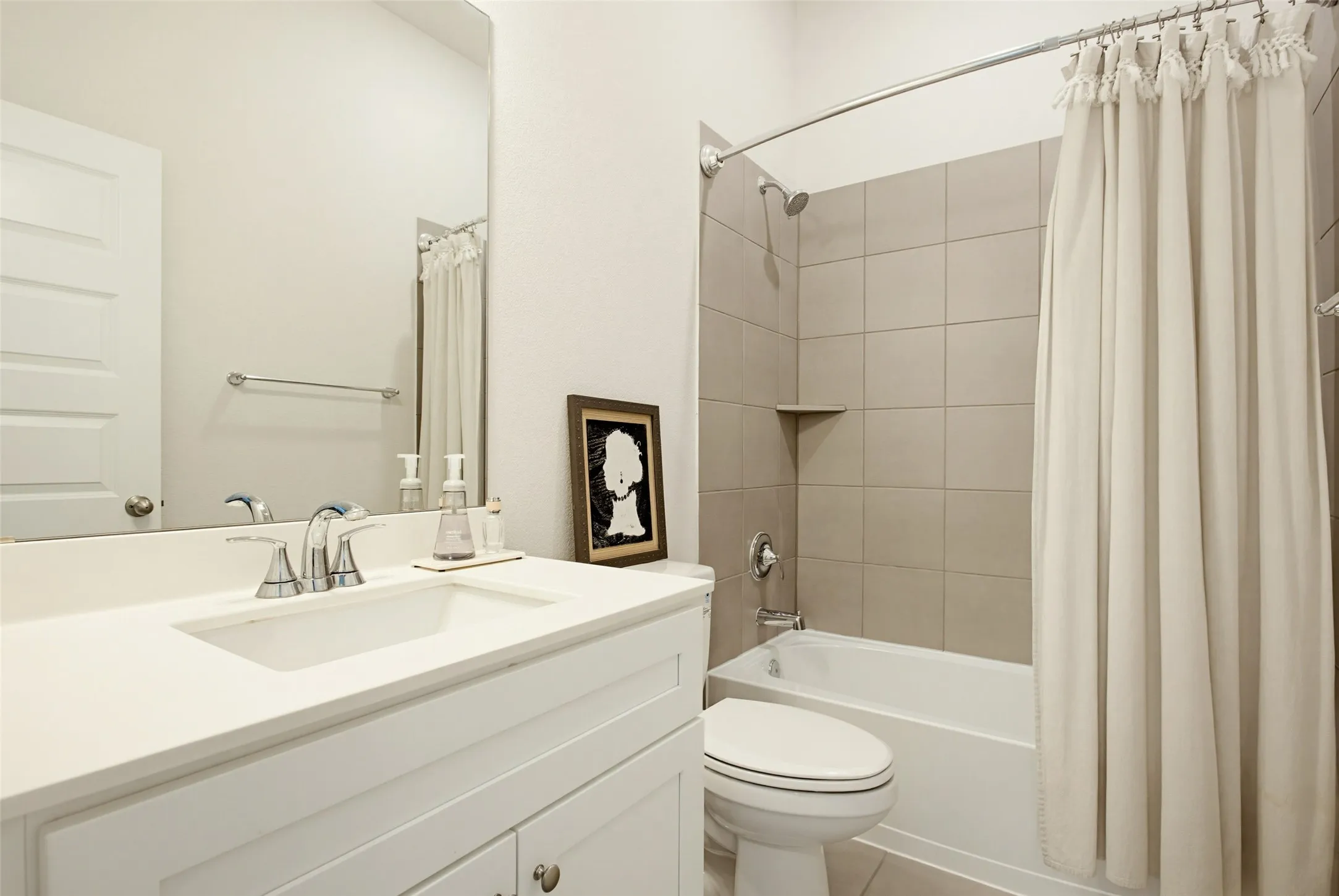 Bathroom featuring a vanity with an integrated sink and chrome faucet, a large wall-mounted mirror, and a full-size tub with square wall tiling and a built-in shelf