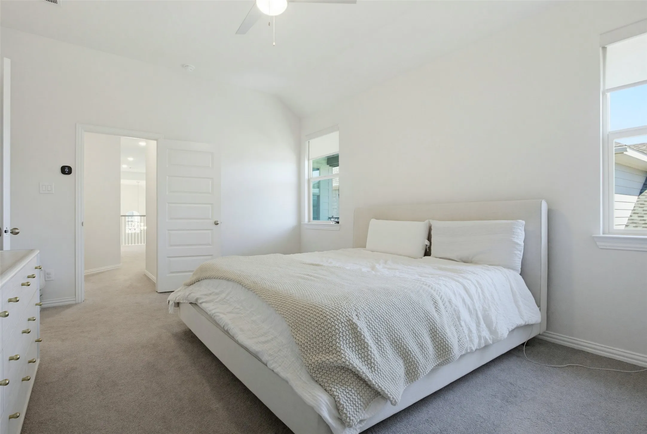 Carpeted bedroom featuring a vaulted ceiling with a ceiling fan, white paneled door, and multiple windows with roller shades