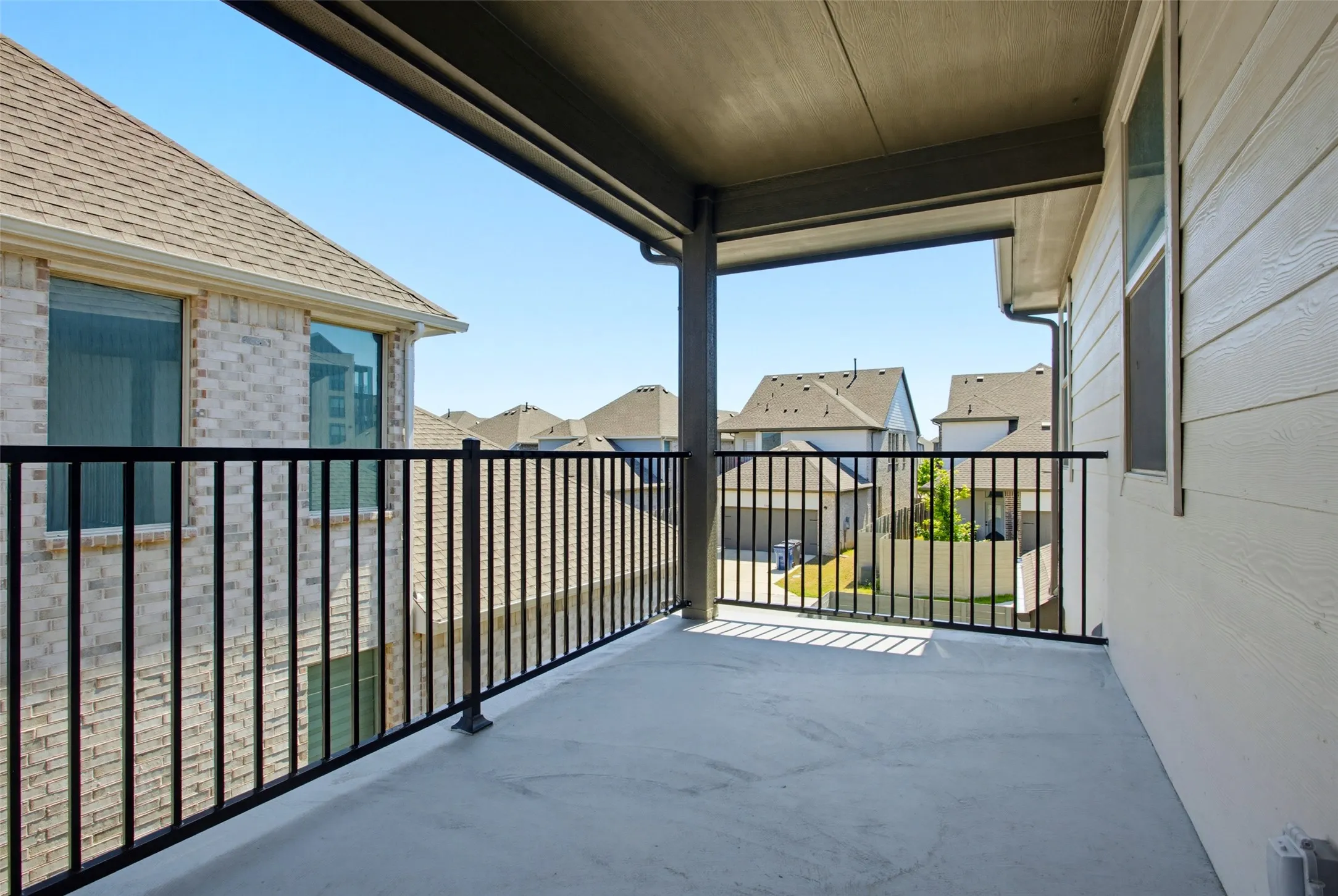 Covered outdoor patio with a concrete surface, black metal railing, and an exterior wall featuring horizontal siding