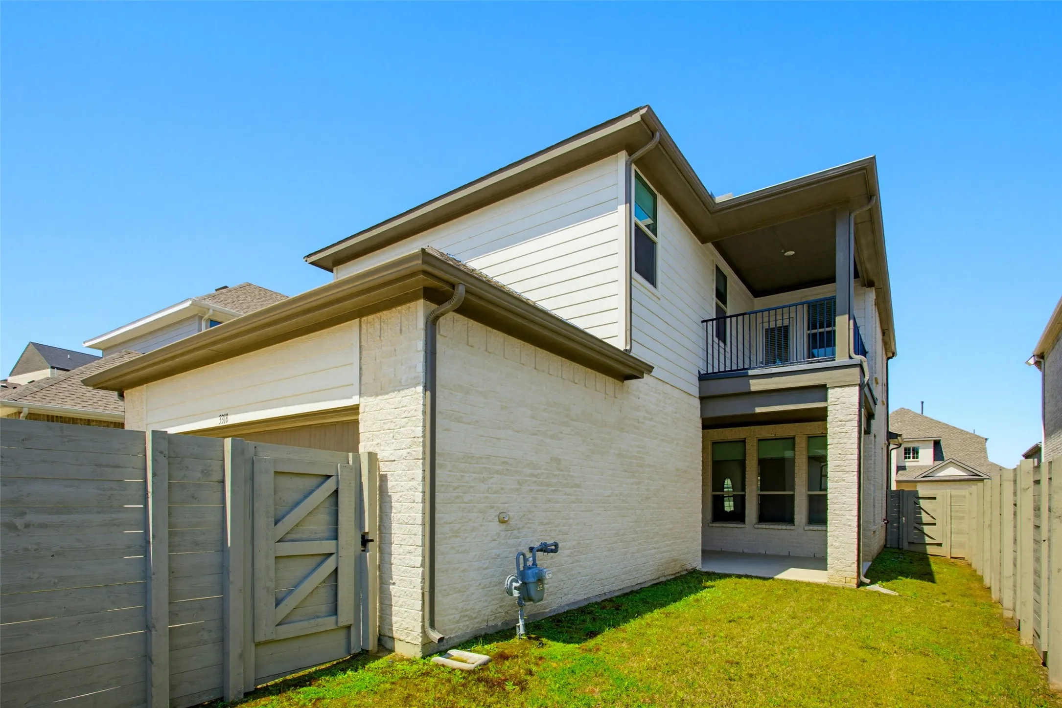 Rear exterior featuring a covered patio, second-story balcony with iron railing, and a private fenced yard