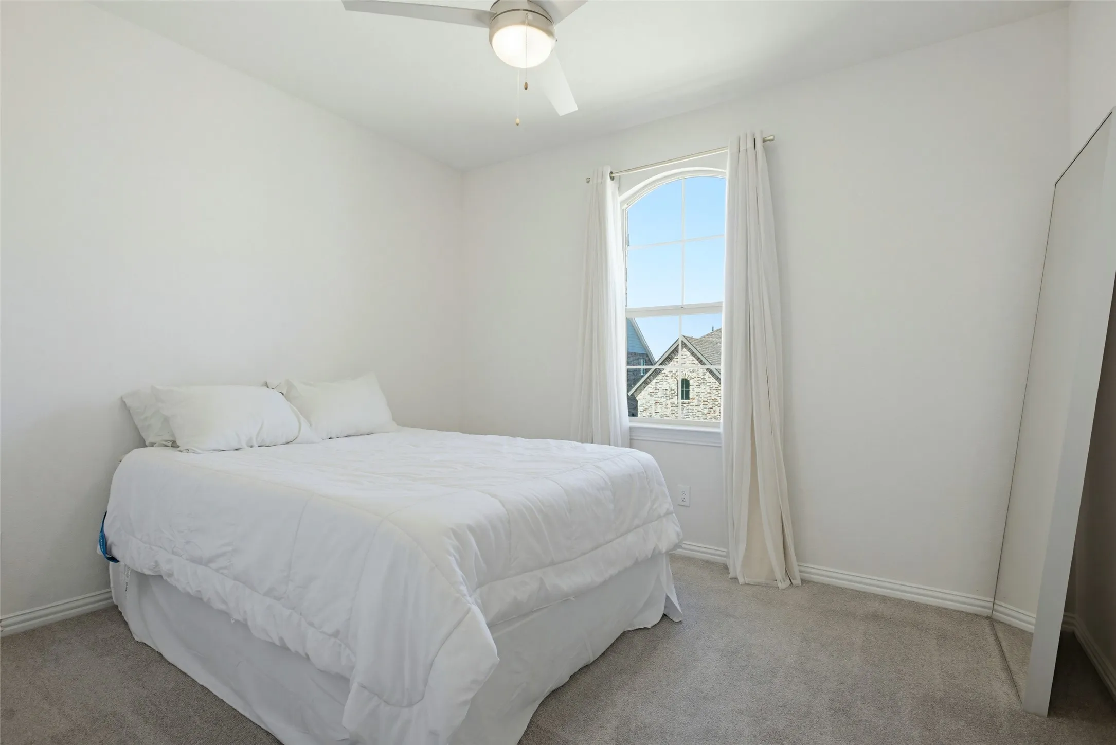 Bedroom featuring a prominent arched window, light gray carpet, and a ceiling fan with integrated lighting