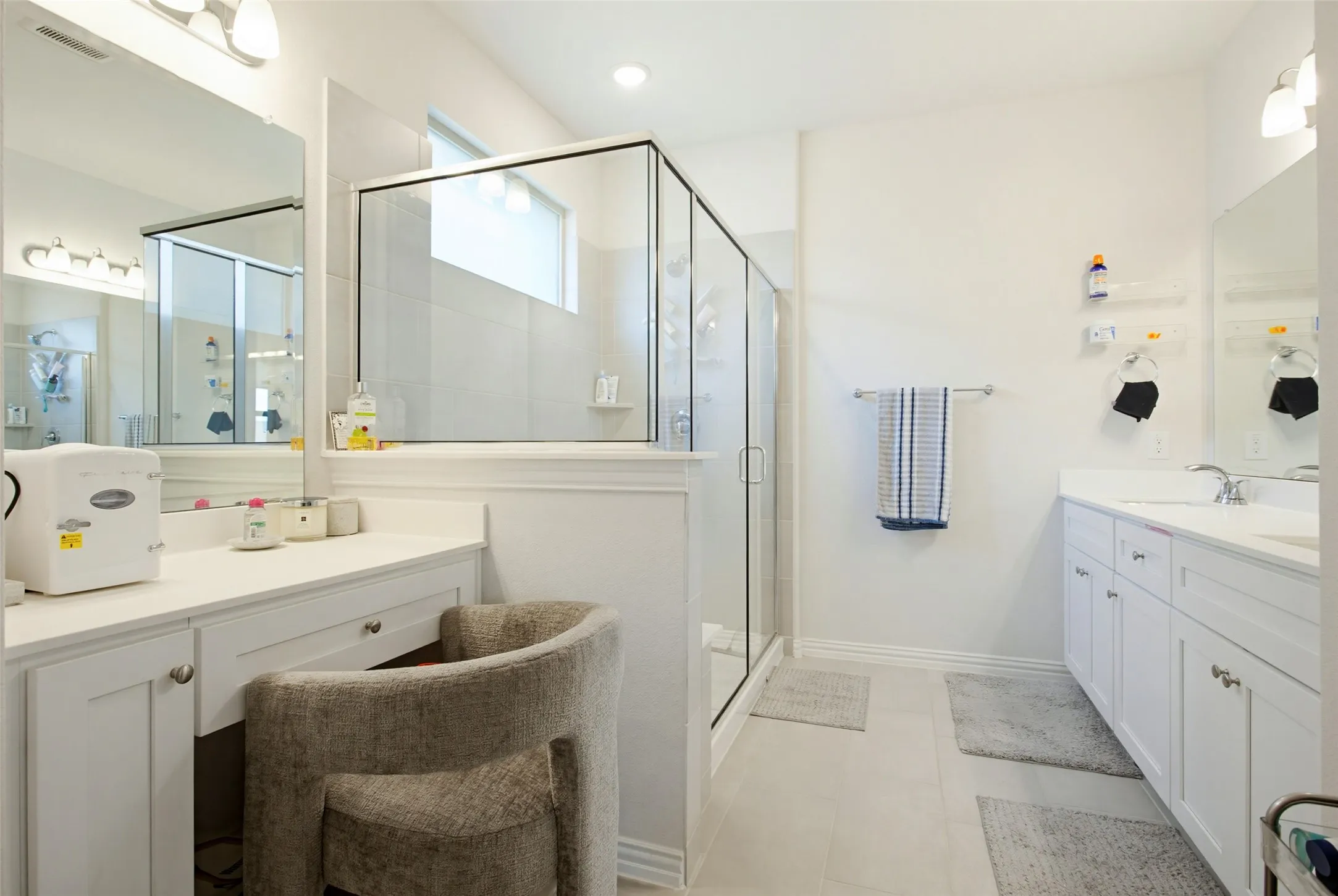 Spacious bathroom featuring a glass-enclosed shower, dual vanities with undermount sinks, a dedicated vanity space, ample cabinet storage, and light-toned tile flooring