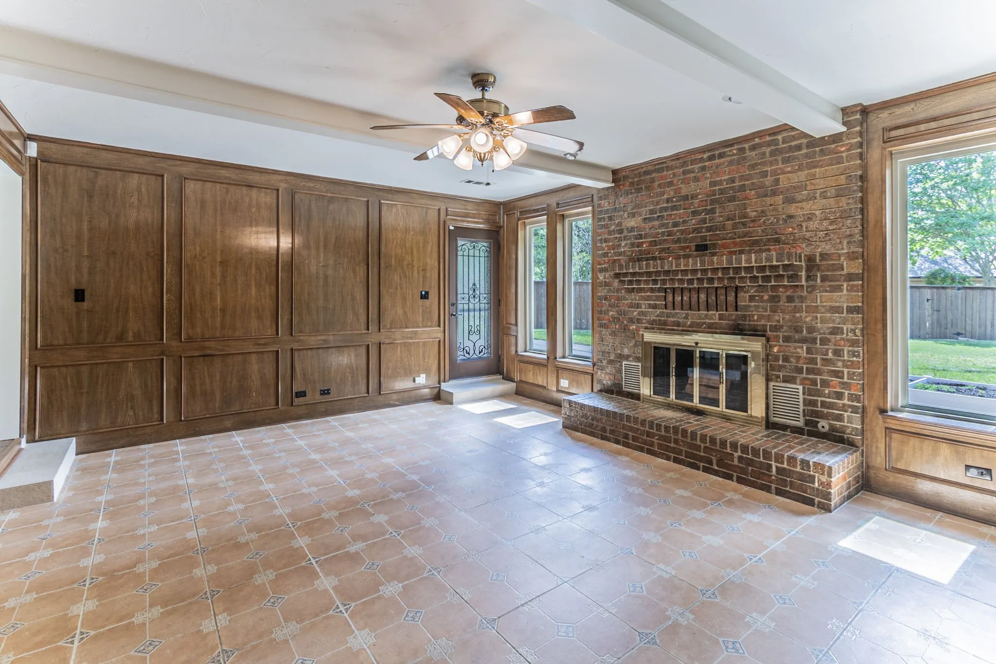 Unfurnished living room with a ceiling fan, wood walls, a fireplace, beam ceiling, and light tile patterned flooring
