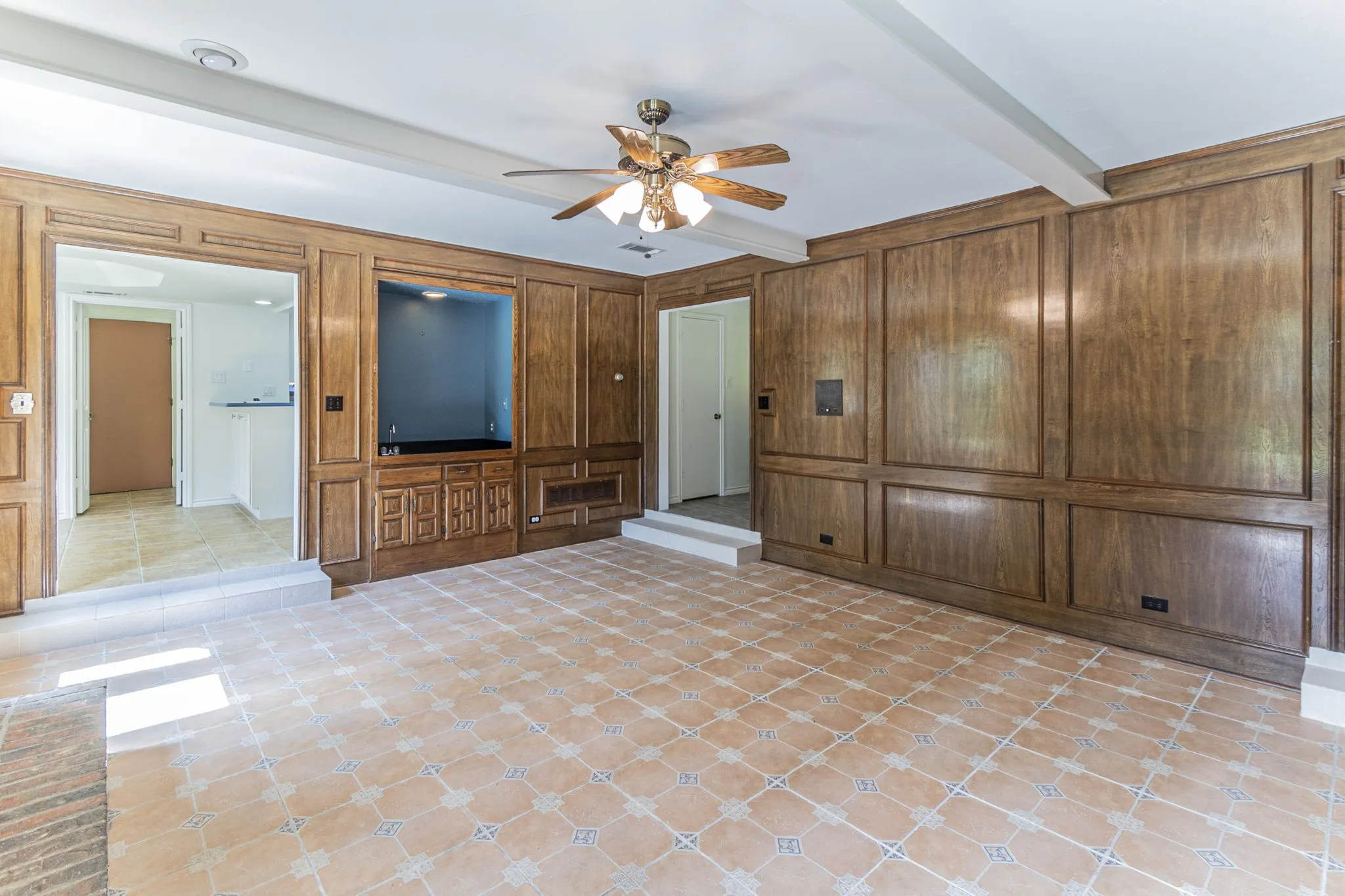 Unfurnished living room with a ceiling fan, beamed ceiling, wood walls, and a decorative wall