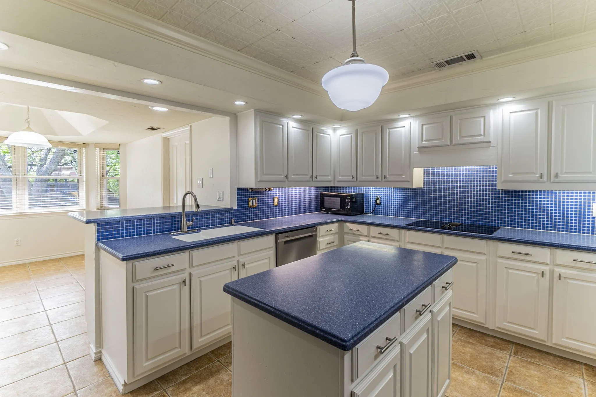 Kitchen with a peninsula, ornamental molding, pendant lighting, dark countertops, and a kitchen island