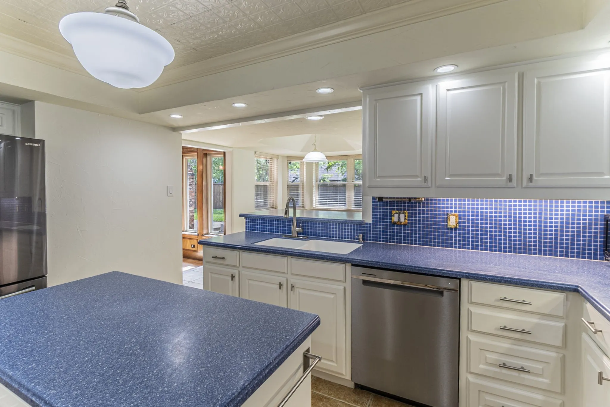 Kitchen with dishwasher, an ornate ceiling, dark countertops, hanging light fixtures, and a kitchen island