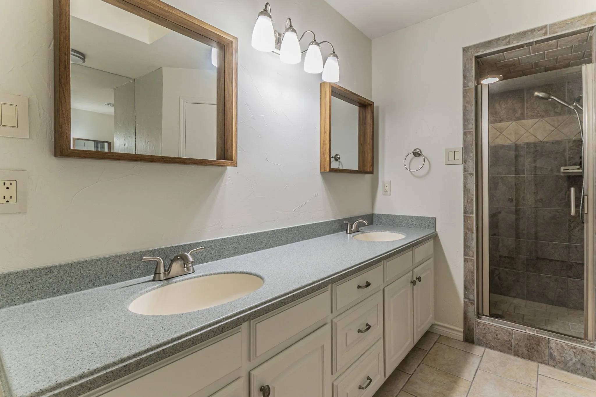 Full bathroom featuring double vanity, a stall shower, and light tile patterned flooring