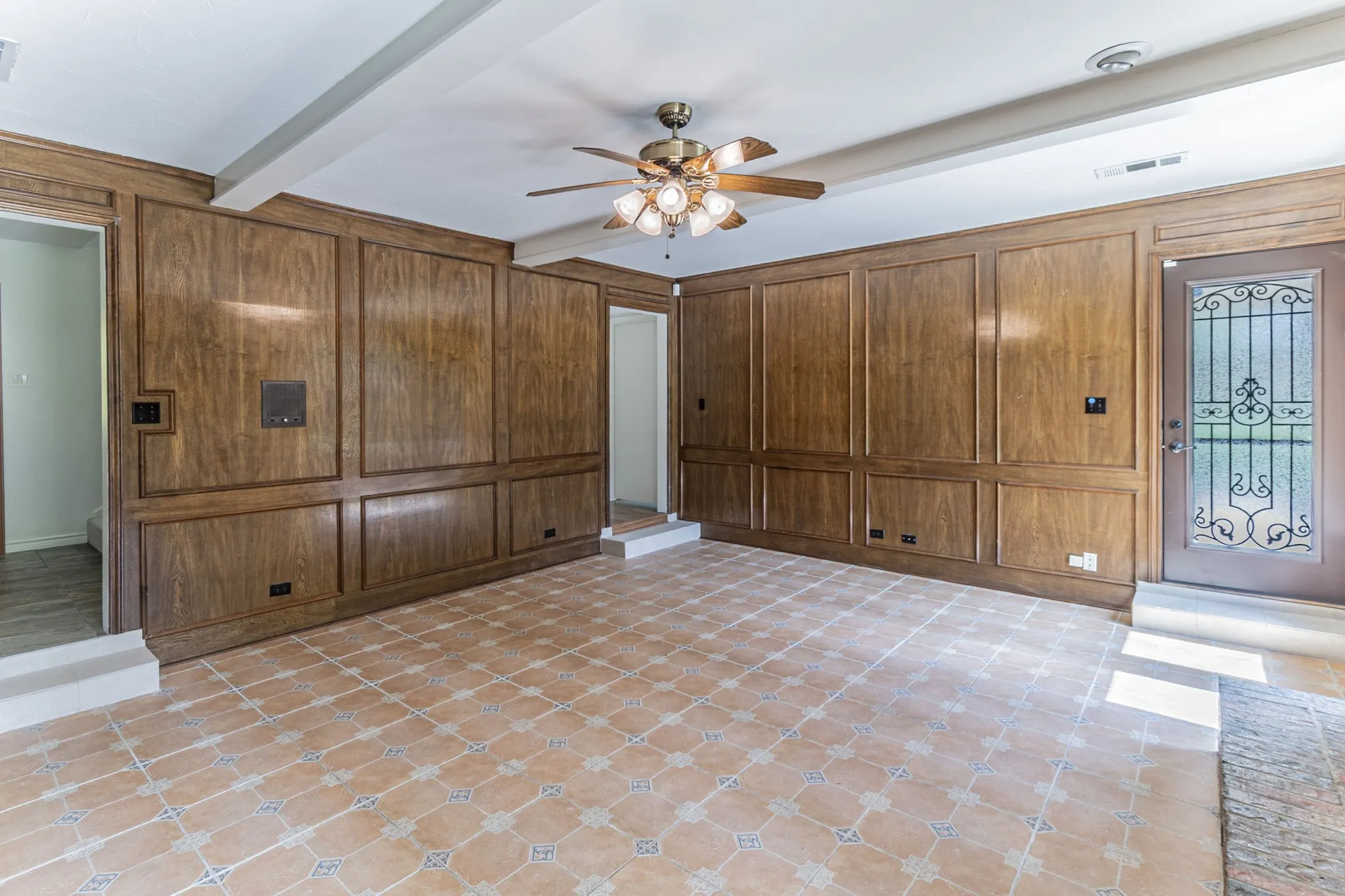Unfurnished living room with a ceiling fan, beam ceiling, and wooden walls