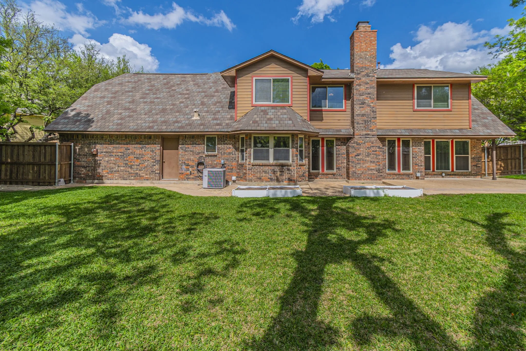 Rear view of property featuring a patio, a fenced backyard, a chimney, brick siding, and a shingled roof