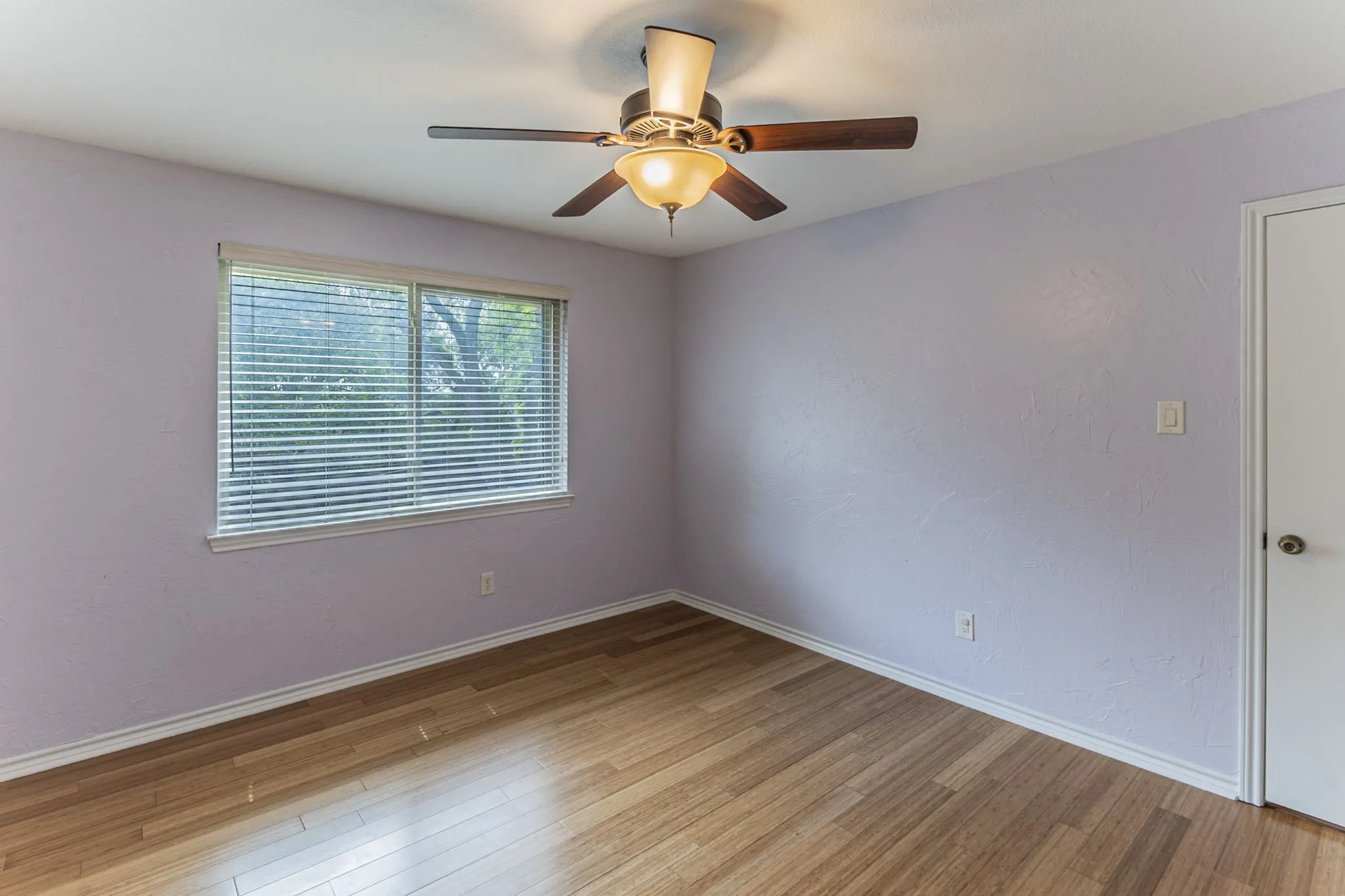 Empty room featuring light wood-style flooring, a ceiling fan, and a textured wall