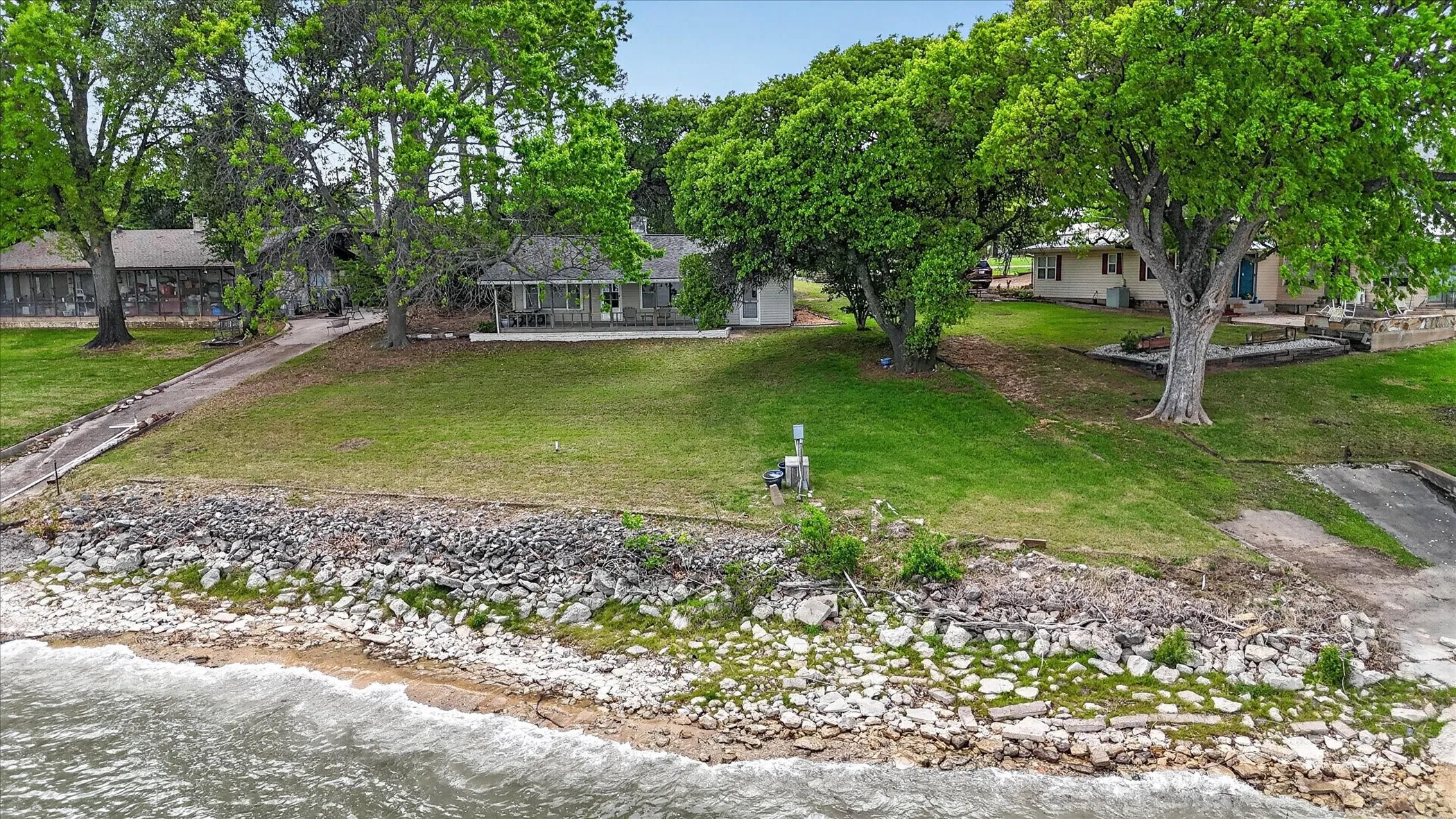 View of waterfront property with mature shade trees and boat ramp.