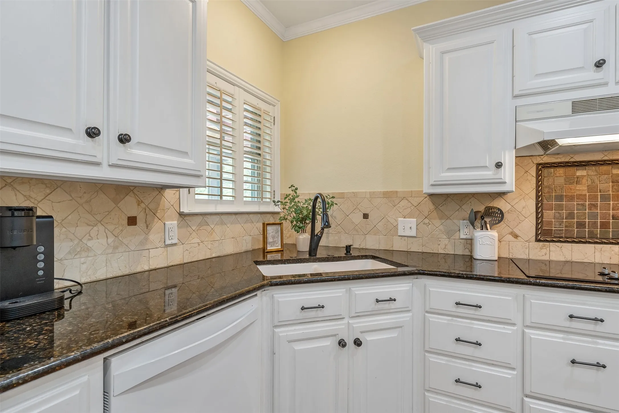 Kitchen with white cabinetry, dark stone counters, dishwasher, and ornamental molding