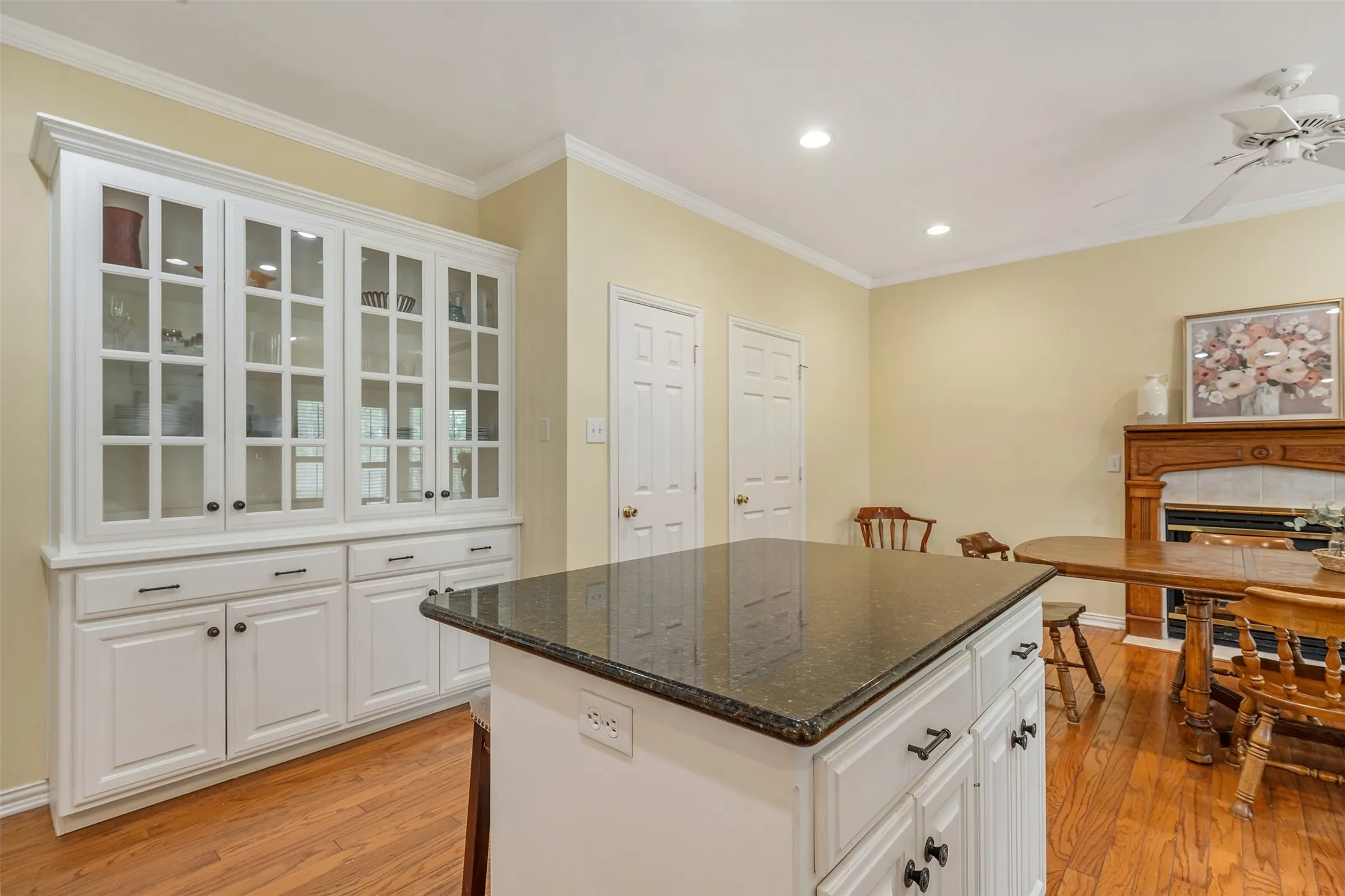 Kitchen with glass insert cabinets, white cabinets, dark stone counters, crown molding, and recessed lighting