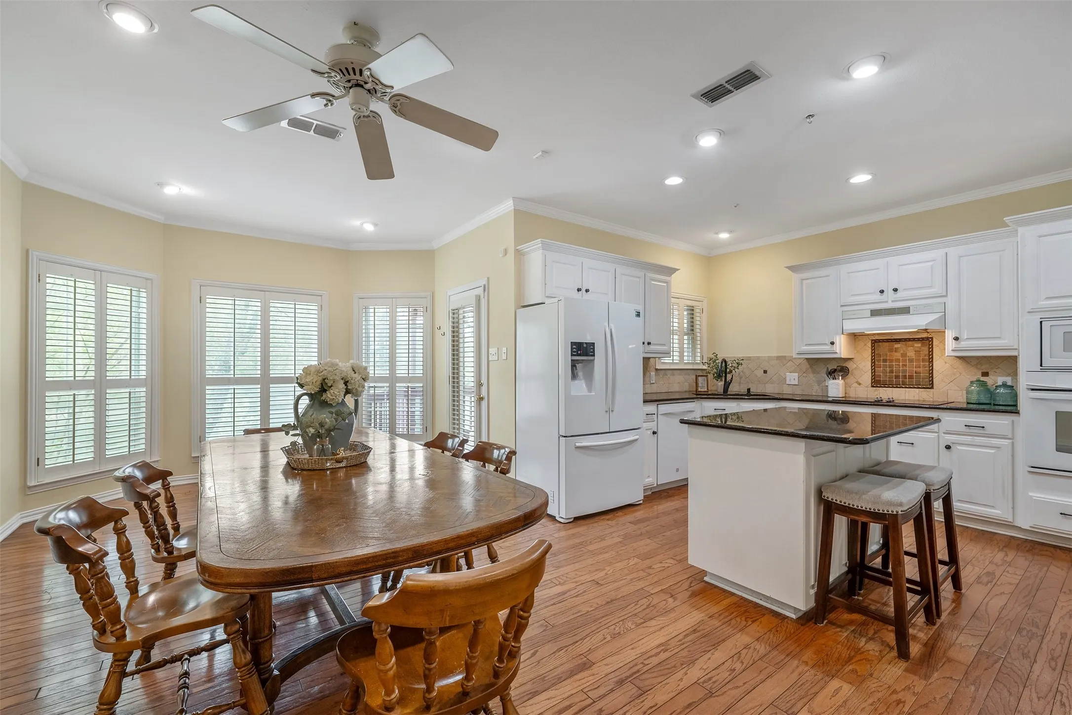 Kitchen with white appliances, light wood-type flooring, white cabinetry, a kitchen island, and recessed lighting