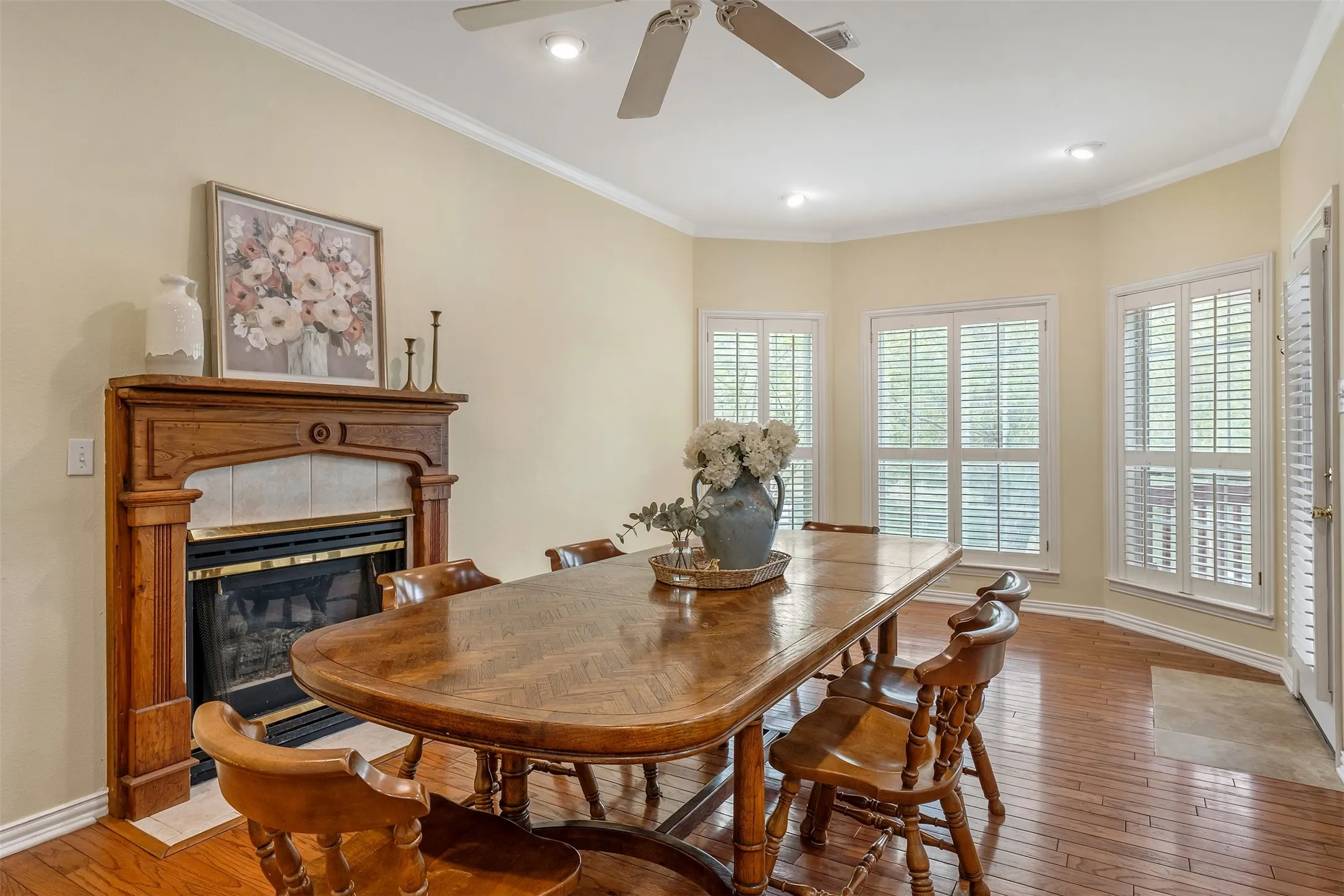 Dining room featuring a tiled fireplace, ornamental molding, wood-type flooring, and ceiling fan