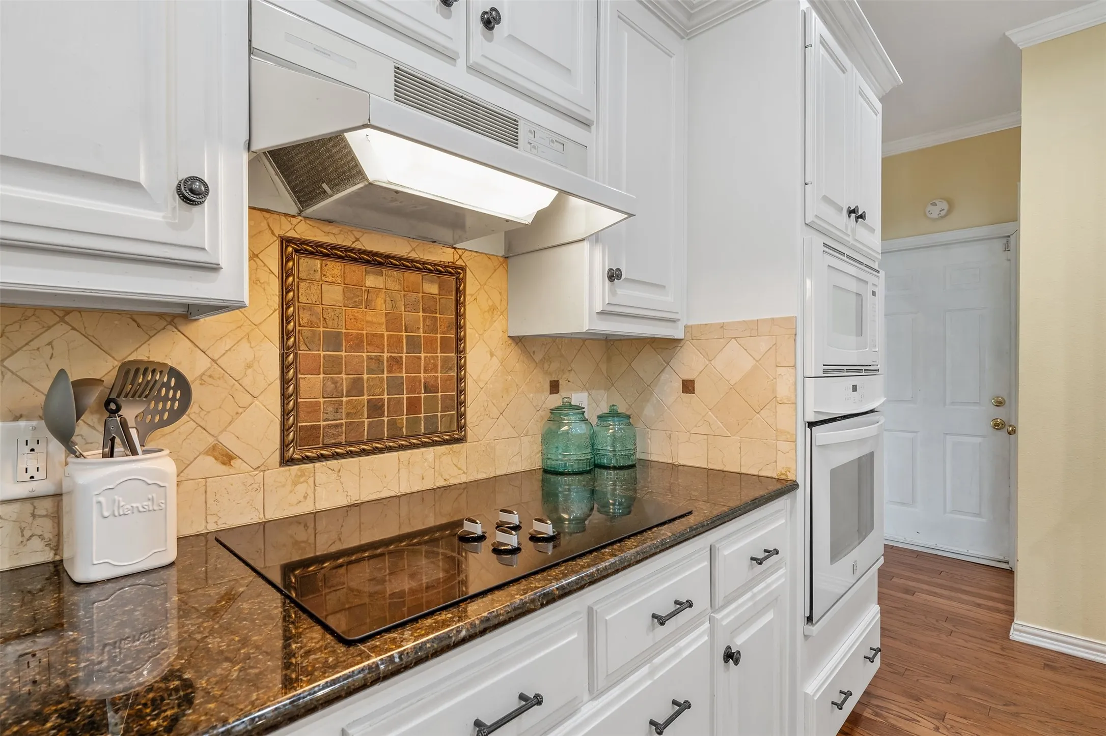 Kitchen featuring crown molding, white cabinets, dark stone countertops, and dark wood-type flooring
