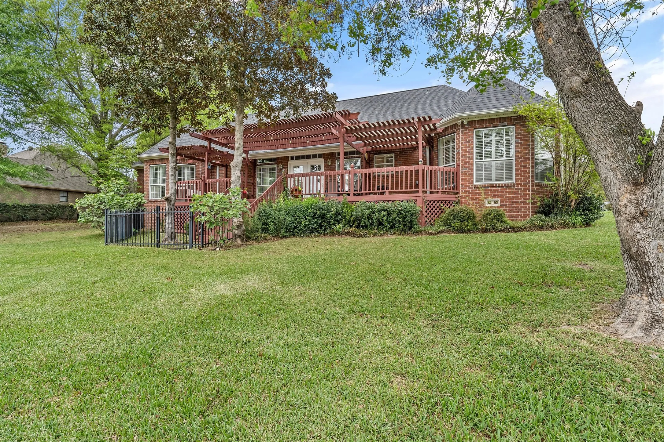 Back of house with brick siding, a deck, roof with shingles, and a pergola