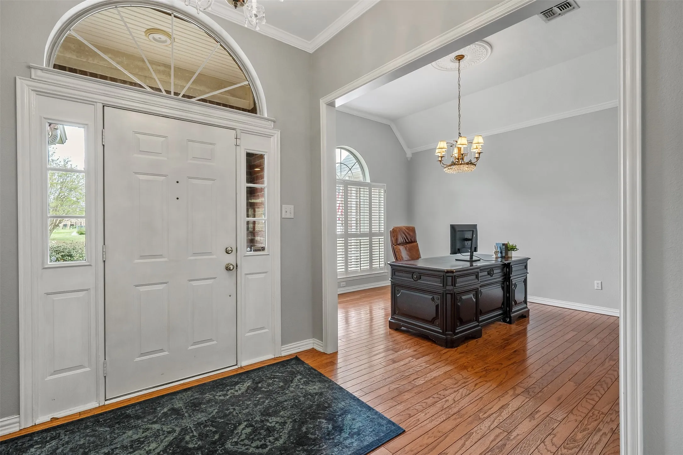Entrance foyer featuring suspended lighting, wood-type flooring, lofted ceiling, and crown molding