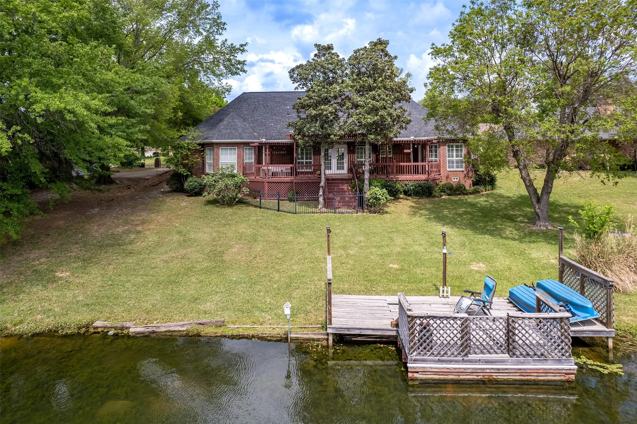 Rear view of house with a lawn, a shingled roof, and a deck with water view