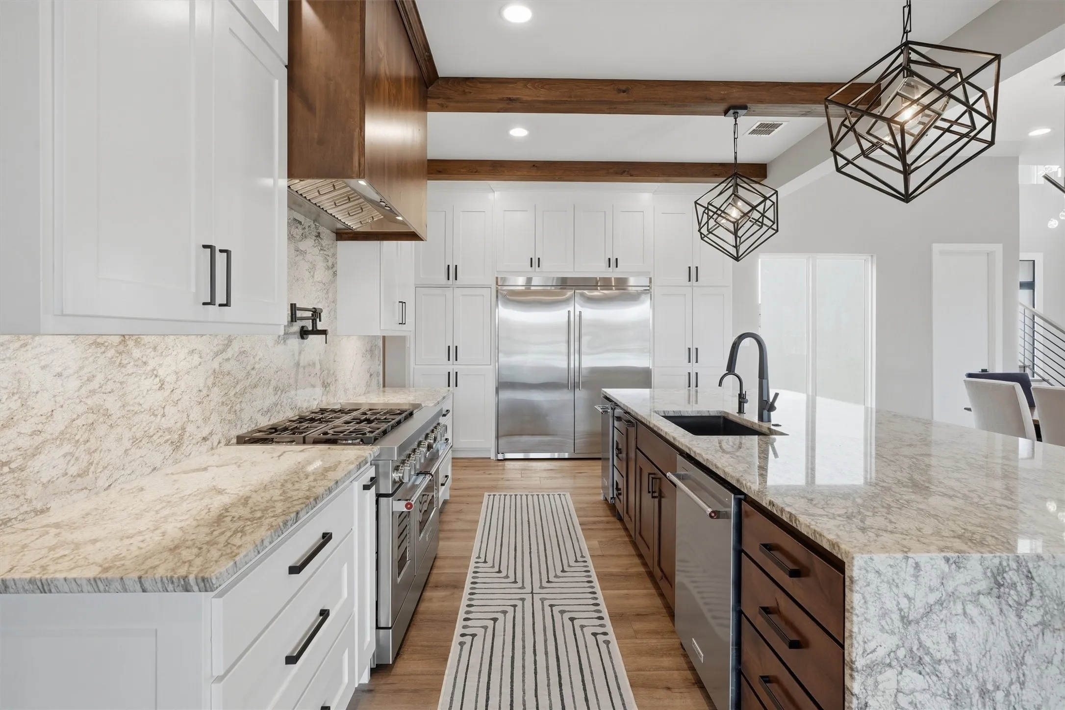 Kitchen featuring two tone color scheme, light stone countertops, premium appliances, decorative light fixtures, and a spacious island