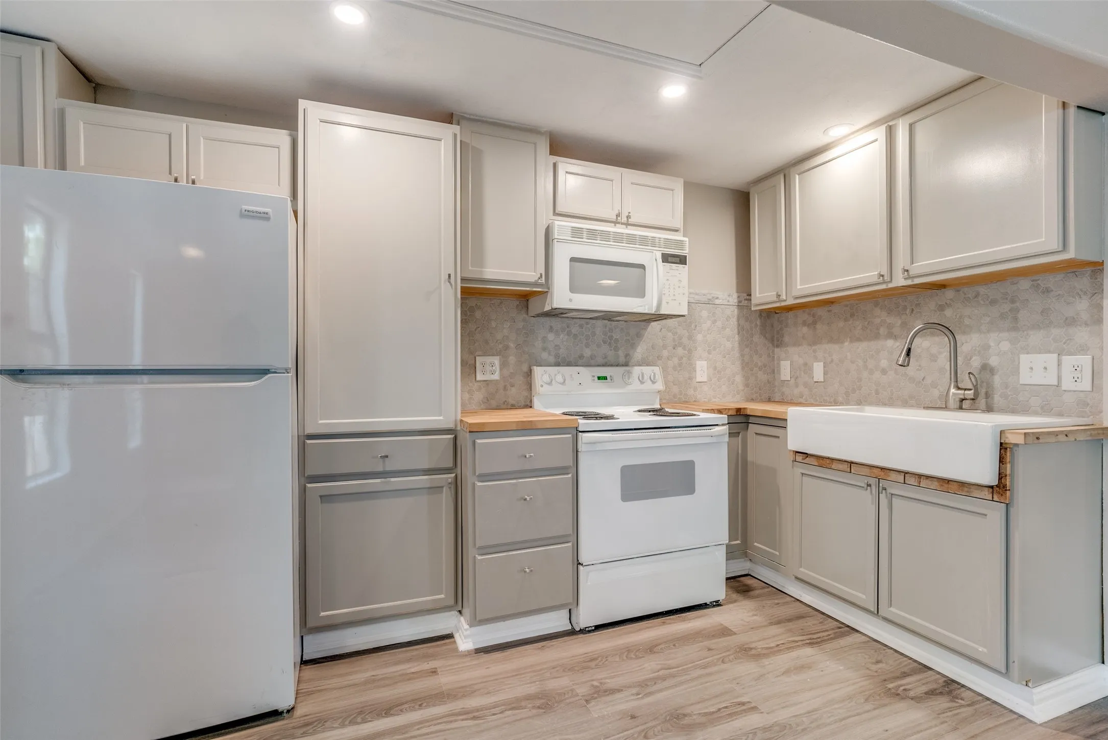 Kitchen with white appliances, light wood-style floors, wooden counters, recessed lighting, and backsplash