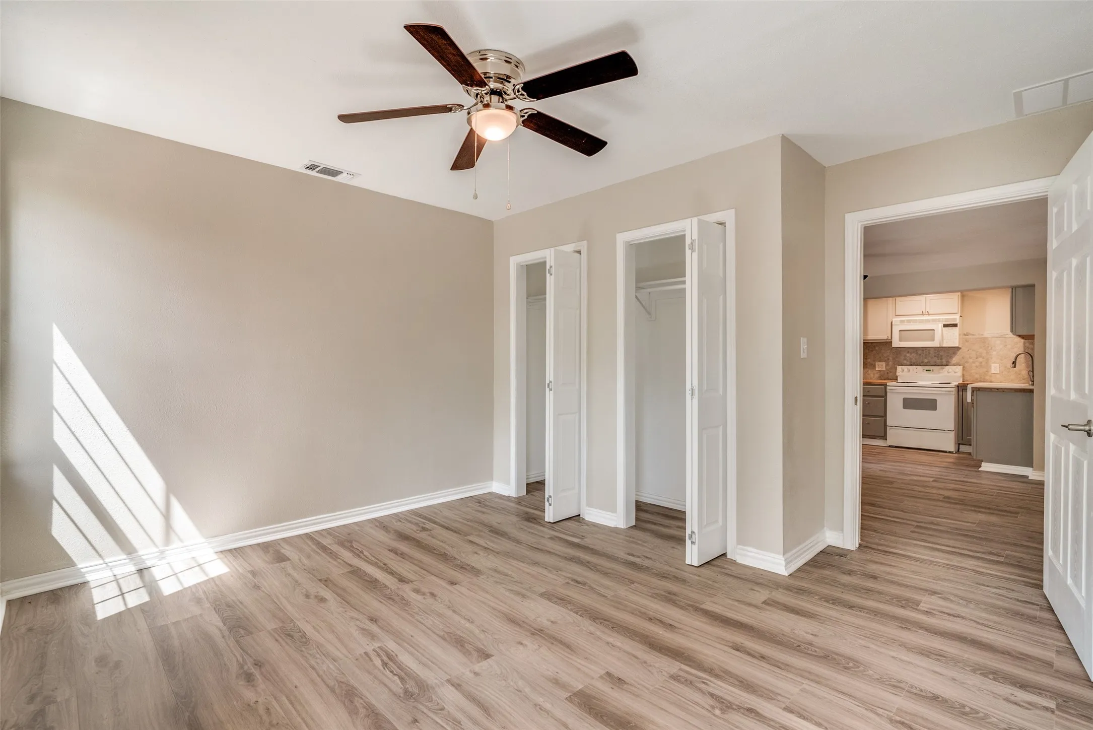 Unfurnished bedroom with multiple closets, light wood-style floors, and ceiling fan