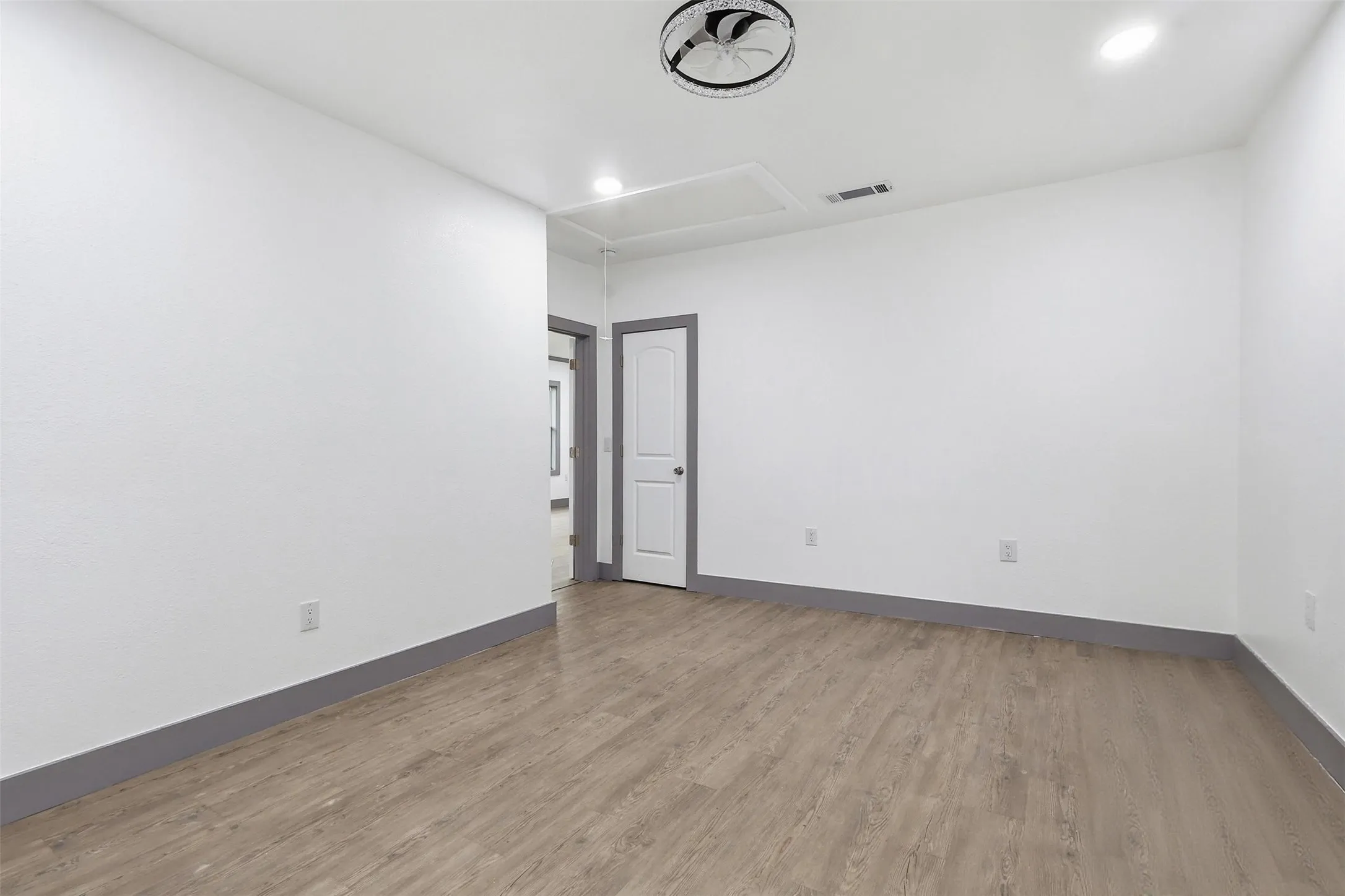 Spacious room featuring wood-finish flooring, white walls, and a contemporary ceiling fixture