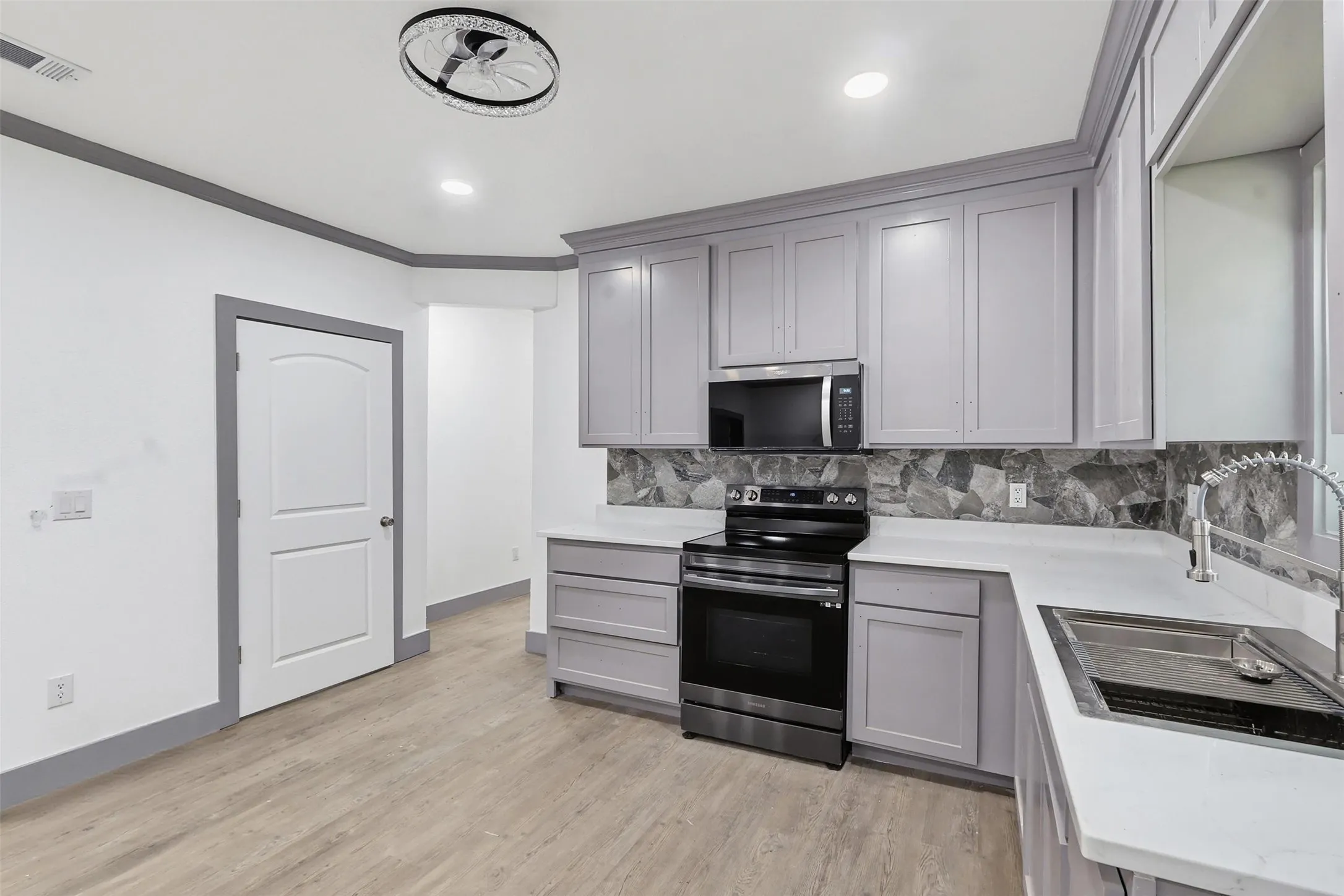 Kitchen featuring light gray cabinetry, stainless steel appliances, a stone-finish backsplash, and light wood-finish flooring