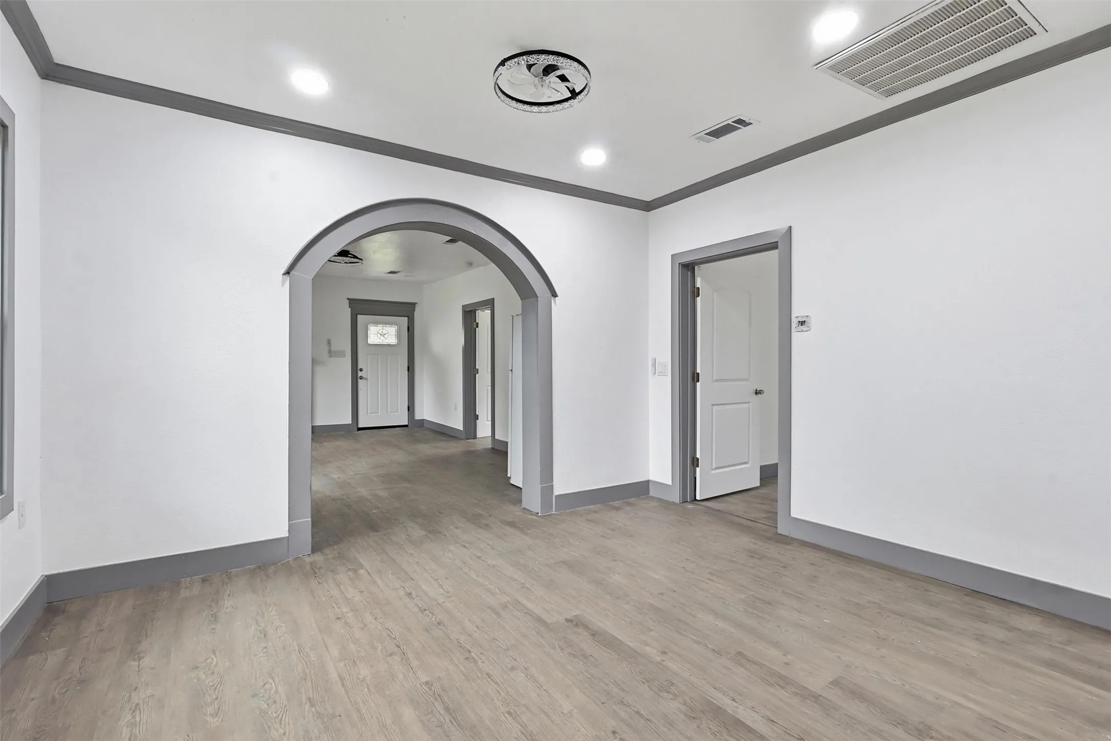 Spacious interior featuring light wood-finish flooring, white walls with contrasting gray trim, recessed lighting, and a decorative ceiling fan