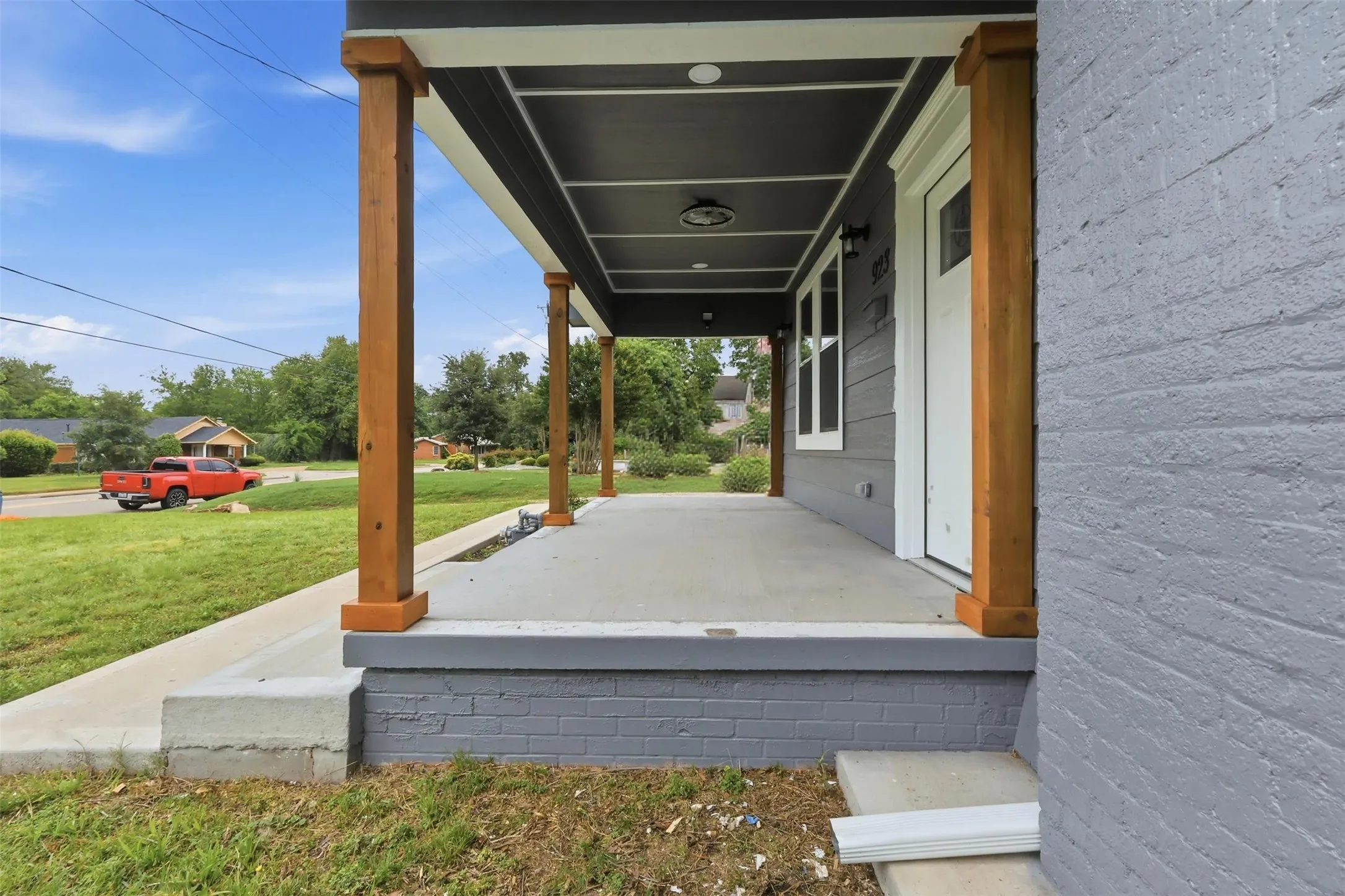 Covered front porch featuring robust wood columns, a gray painted brick foundation, and a concrete surface