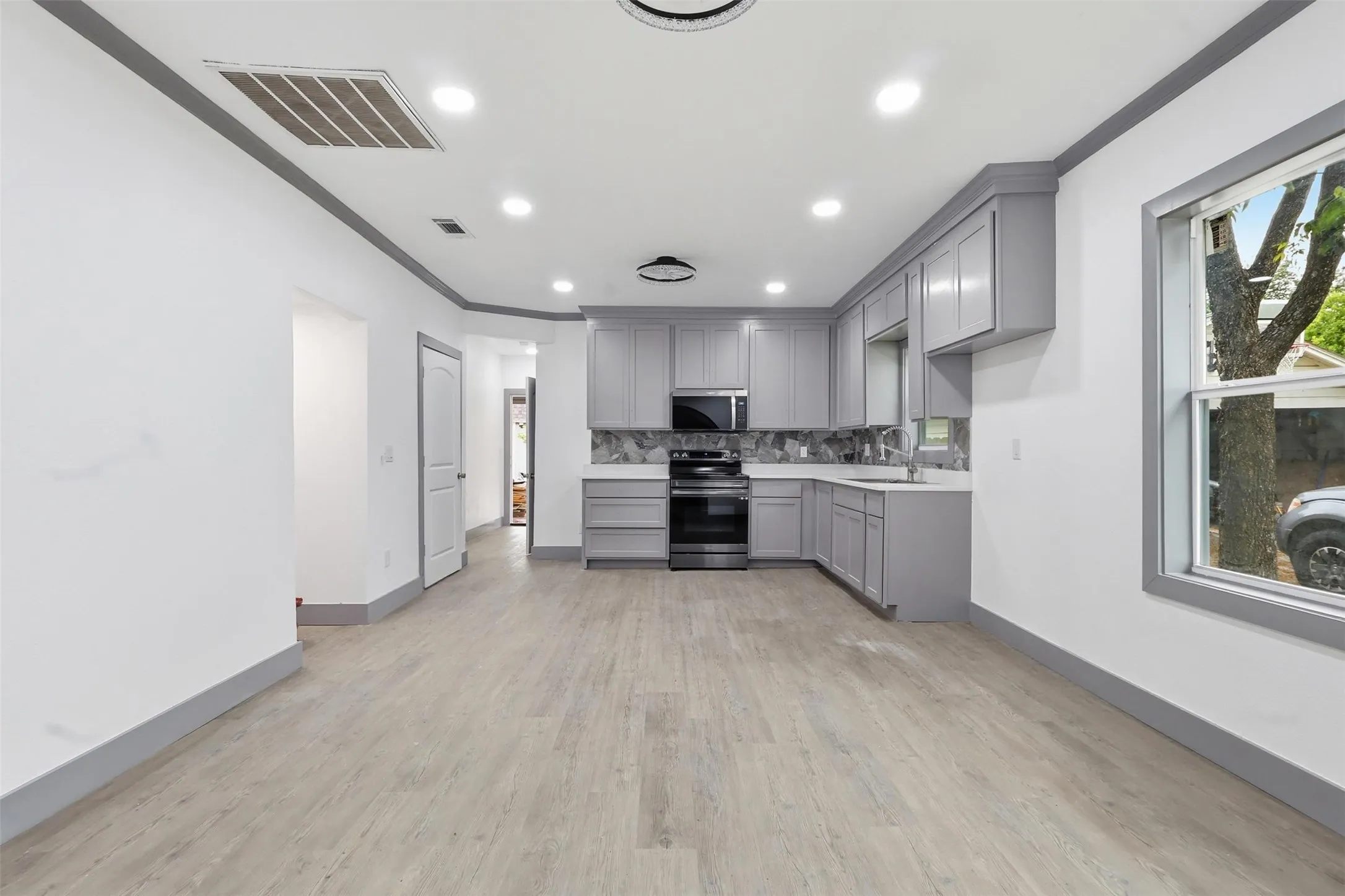 Modern kitchen featuring light gray cabinetry, stainless steel appliances, a patterned tile backsplash, and light wood-finish flooring